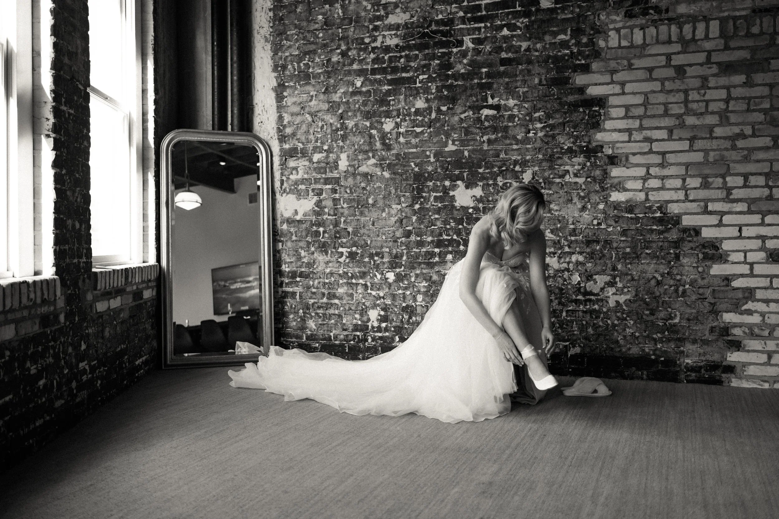 Black and white wedding portrait of a bride putting on her wedding shoes at Oxford Exchange in Tampa, Florida.