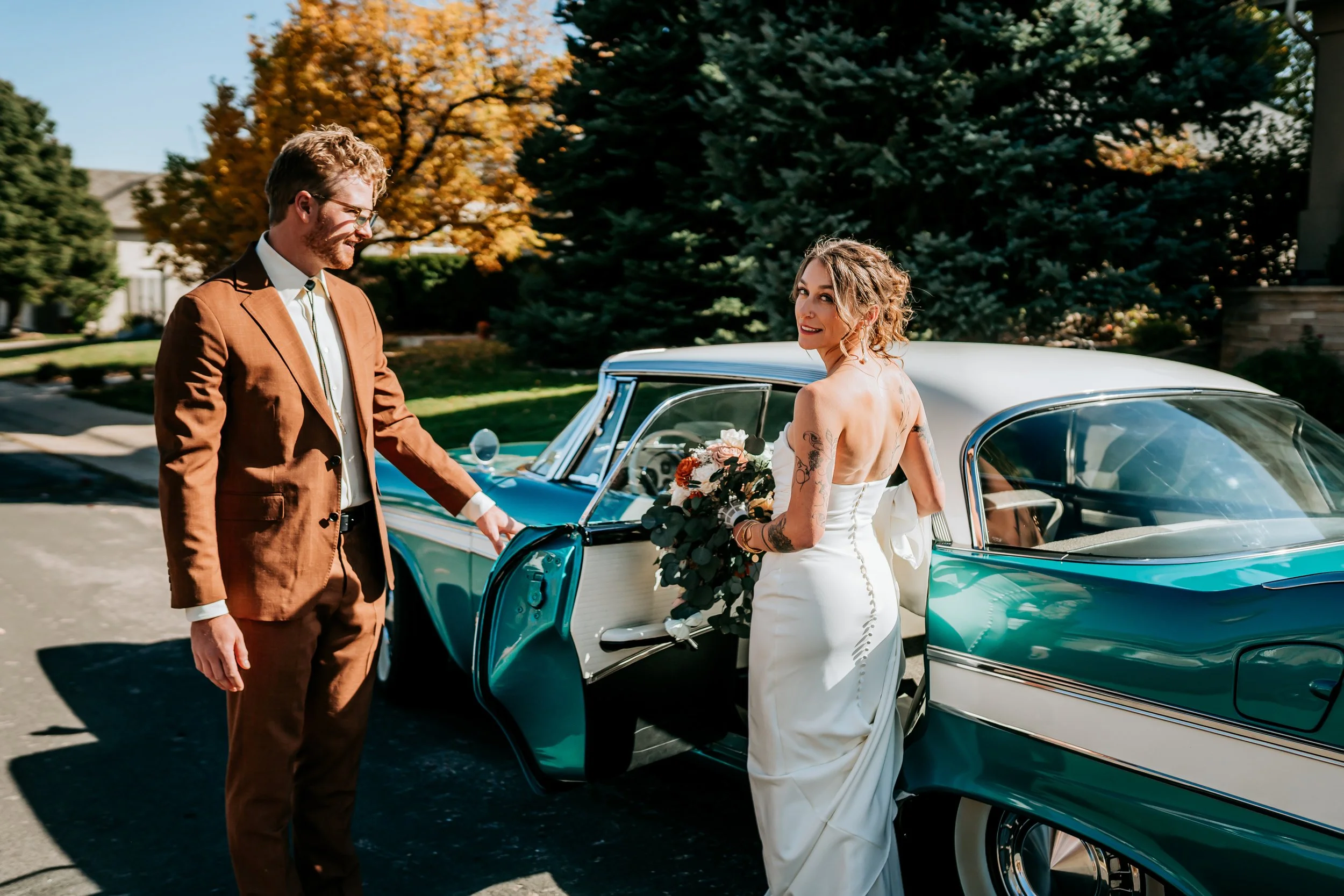 A collection of jewelry, including rings, a necklace with a heart charm, earrings, and a watch, along with a bottle of perfume and white high-heeled sandals, arranged on a white surface with sunlight casting shadows.