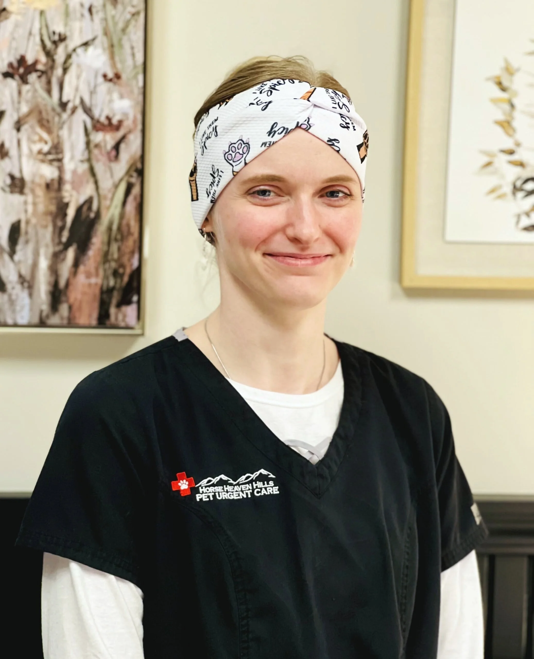 Person in black scrubs with "Horse Heaven Hills Pet Urgent Care" logo wearing a white headband, standing indoors.