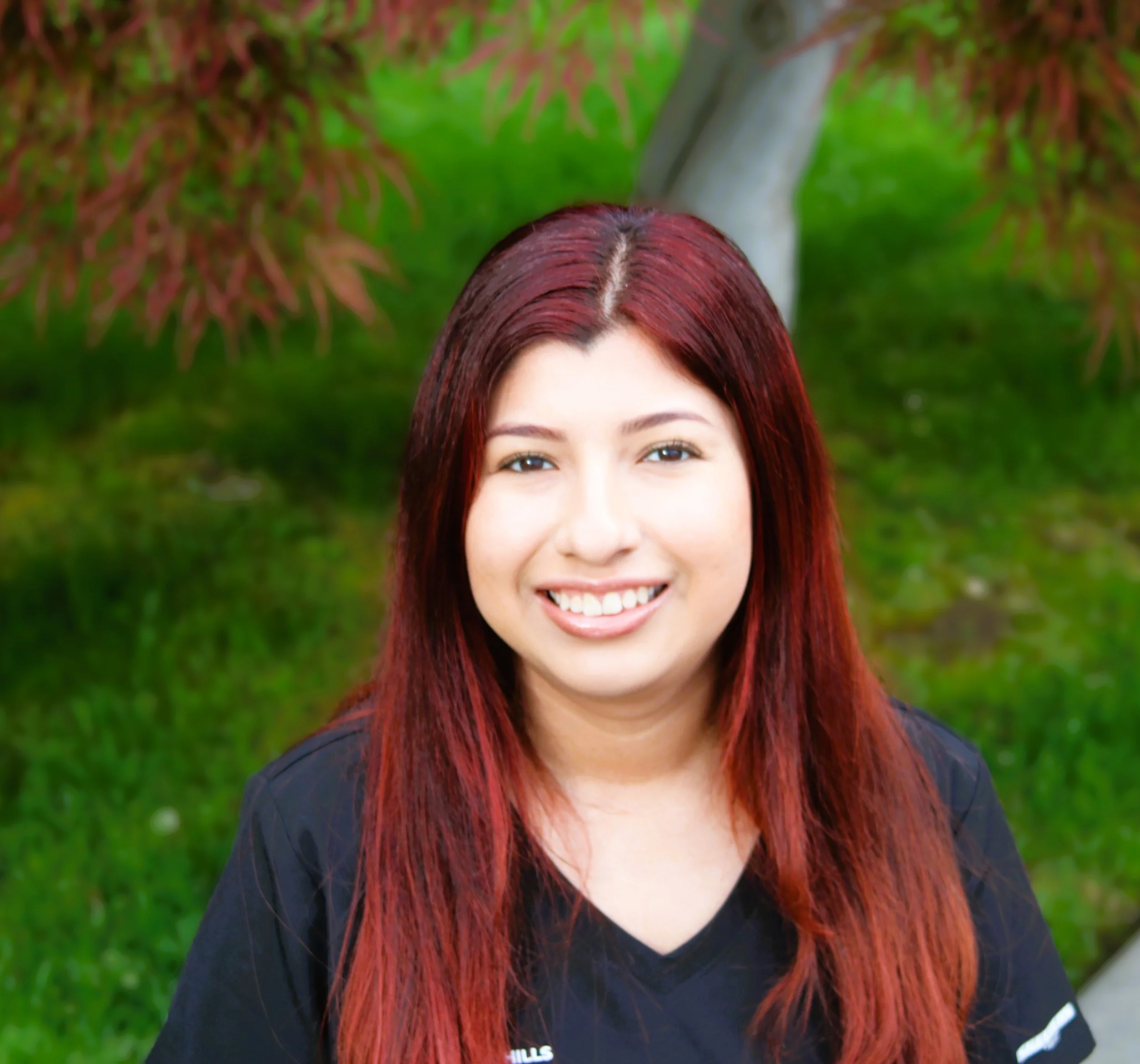 Healthcare professional wearing black scrubs and a stethoscope, smiling in a clinical setting.