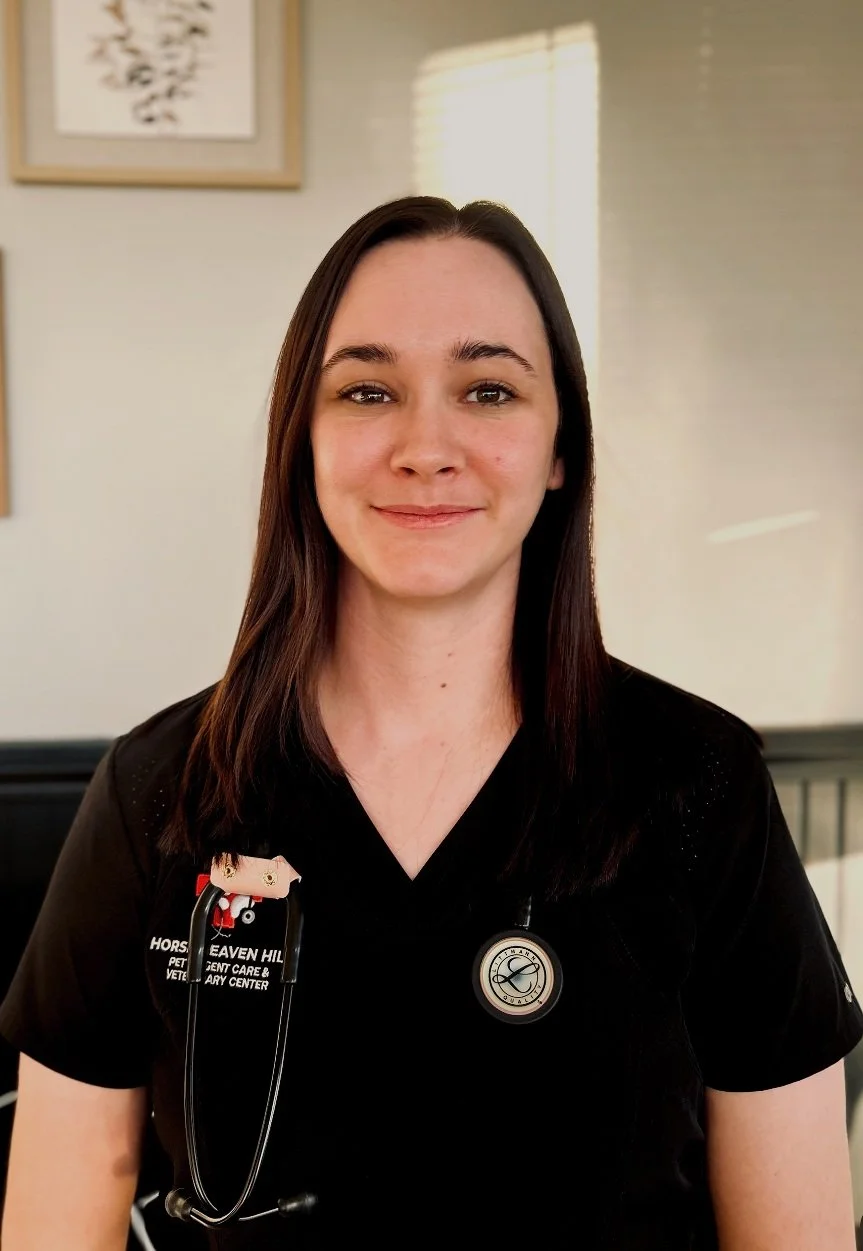 Smiling person wearing a black medical uniform with a stethoscope, standing indoors.