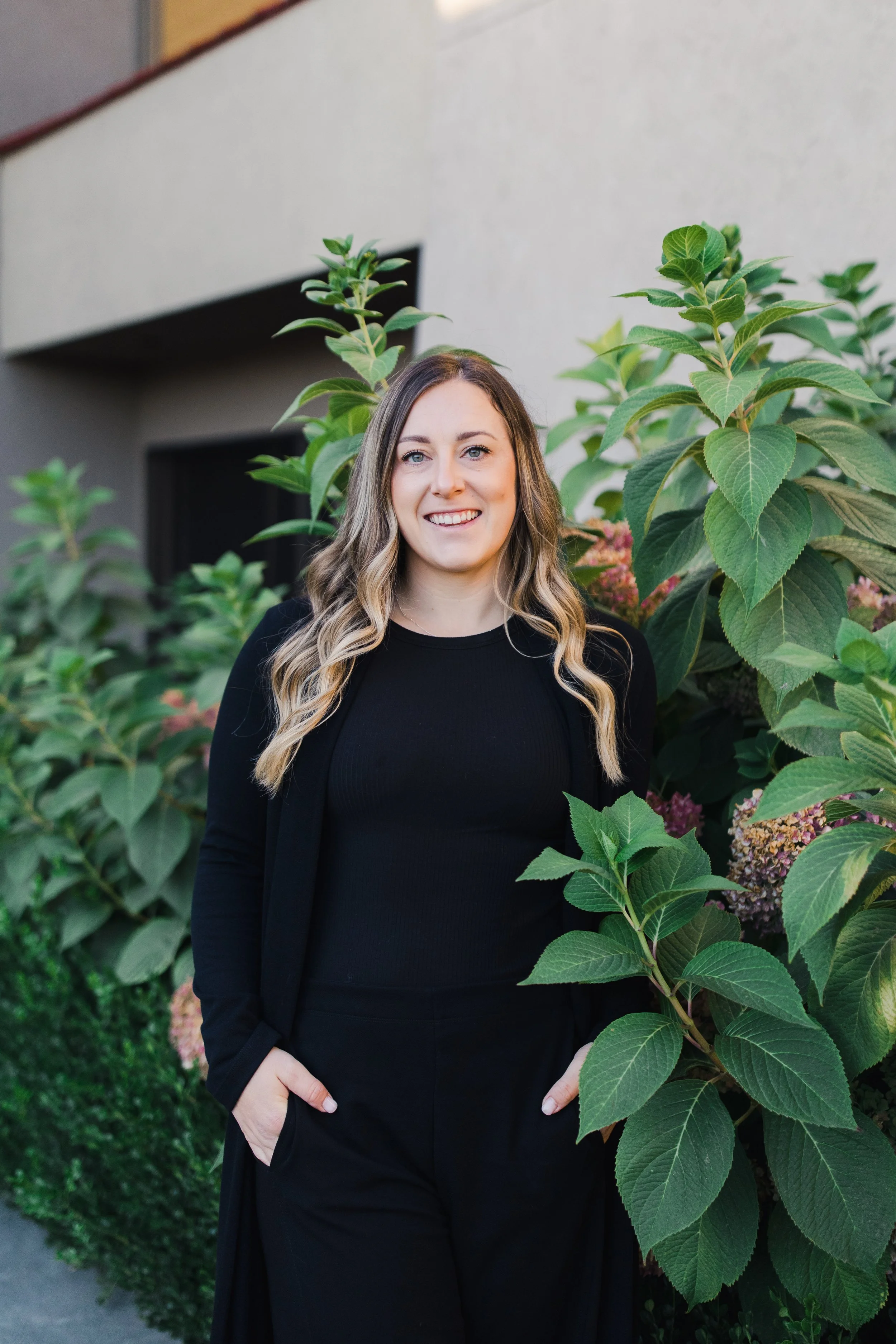 Woman in black blouse standing in a forest with trees and grass in the background.