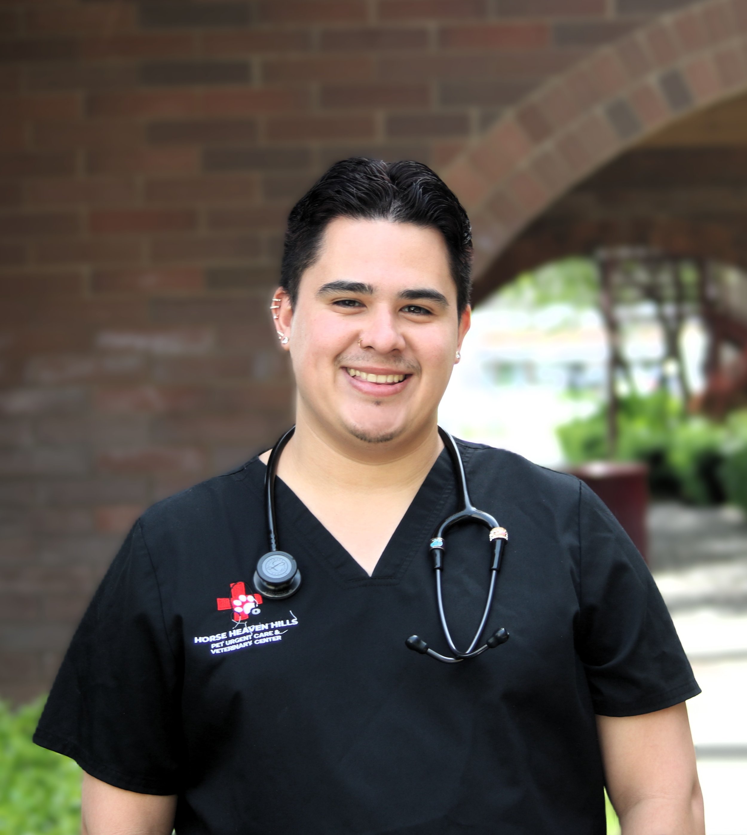 Person smiling, wearing a black scrub top, neutral background with framed art.