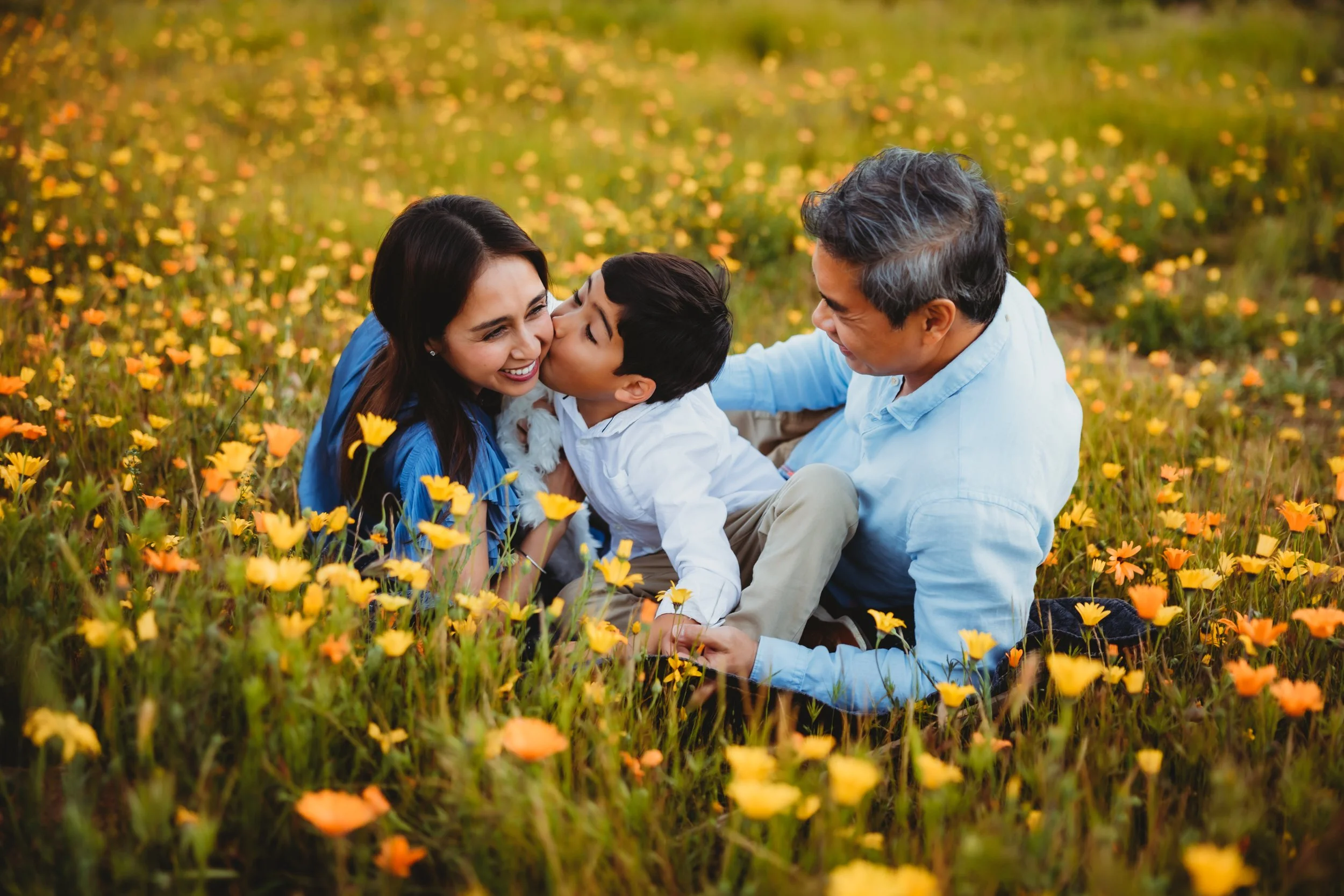 Family of three laying on a field of yellow and orange flowers
