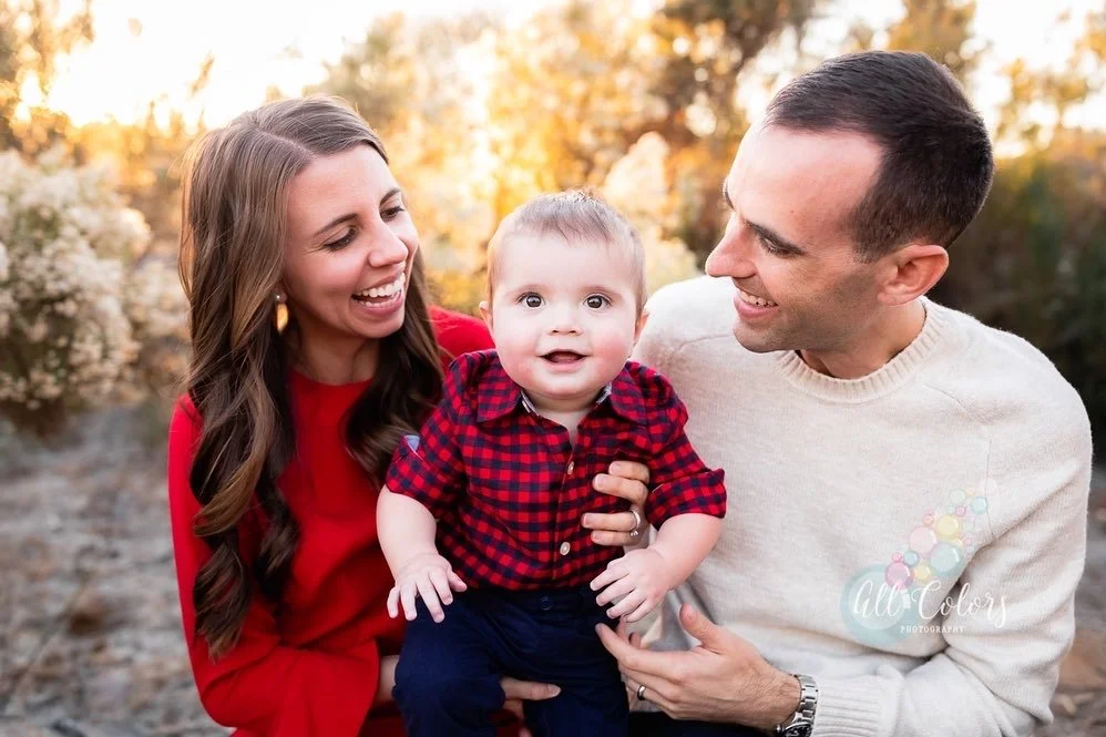 Husband and wife holding their baby boy wearing a red and black plaid shirt.