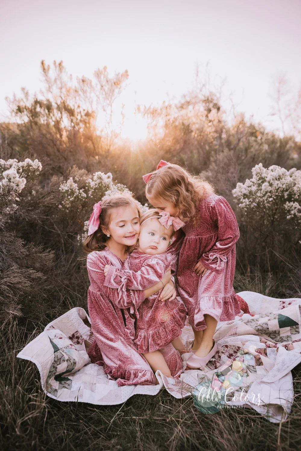 three sisters wearing a mauve pink dress standing on a quilt