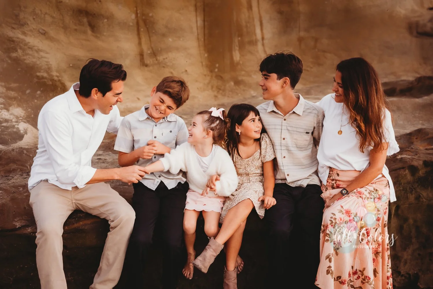 family of six sitting on a beach rock and laughing