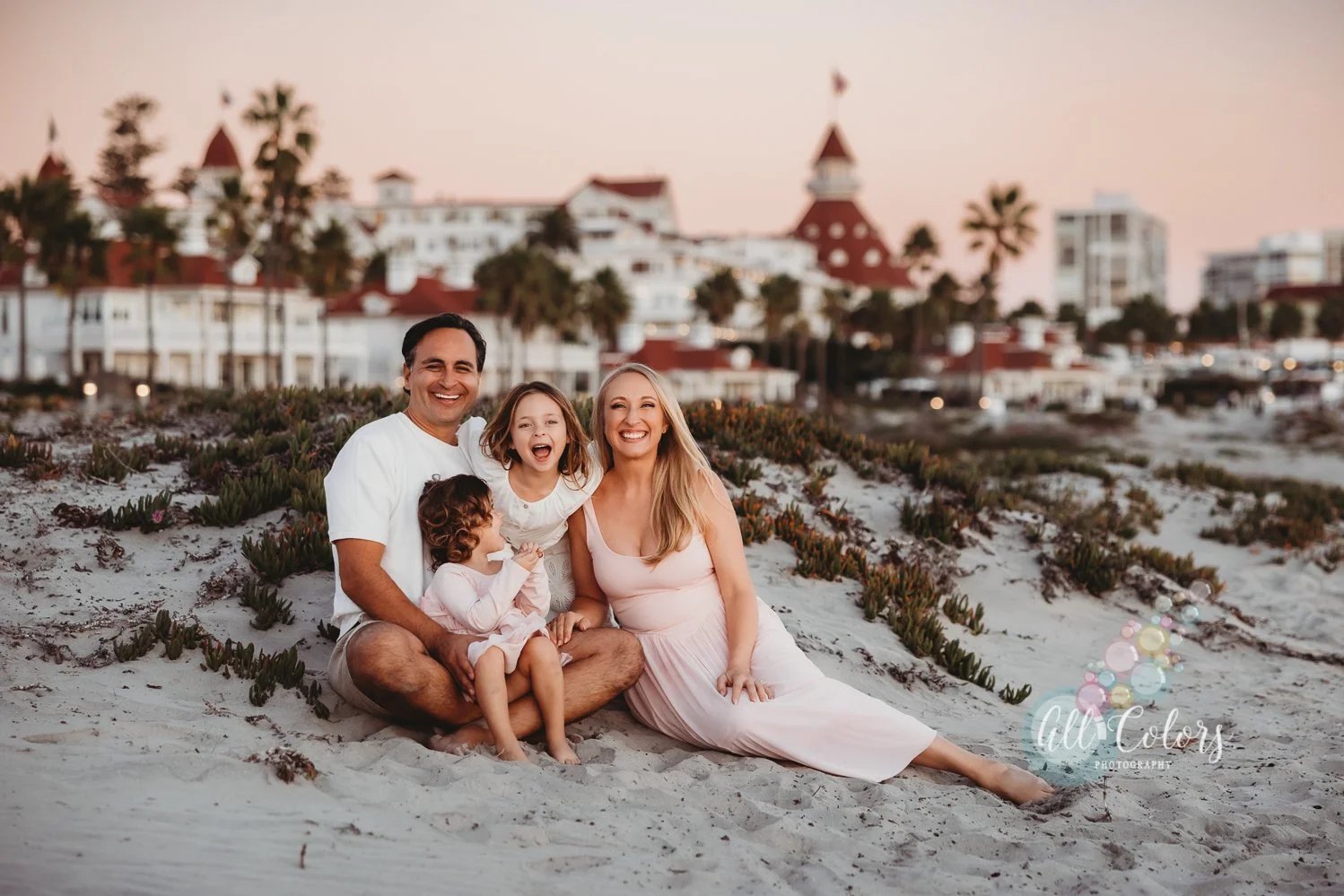 couple and two daughters sitting on the sand in front of the Hotel del Coronado