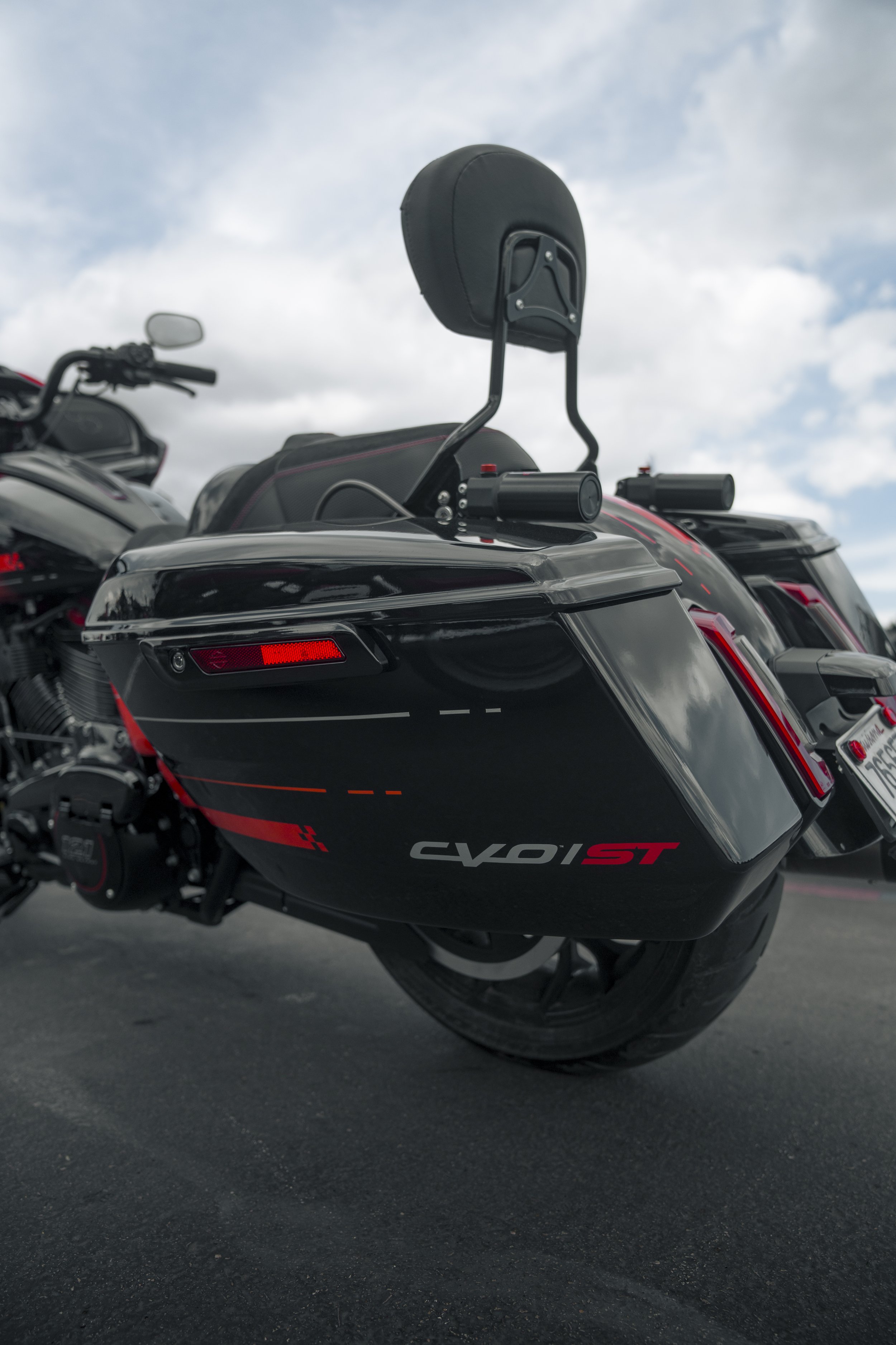 Close-up of a black motorcycle with a sidecar, showing the rear wheel and part of the body, with a cloudy sky in the background.