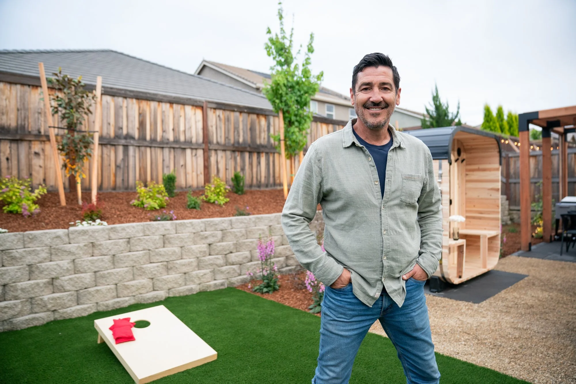 HGTV's Jonathan Knight in the finished Roseville backyard with cornhole lawn, sauna, and modern pergola designed by Palmatum Landscape Design