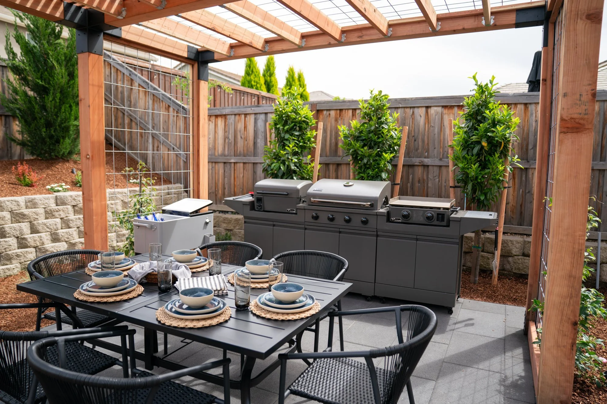 After: modern pergola with outdoor kitchen, grill station, and dining area with citrus trees on wire trellises - HGTV Crashers backyard in Roseville, CA