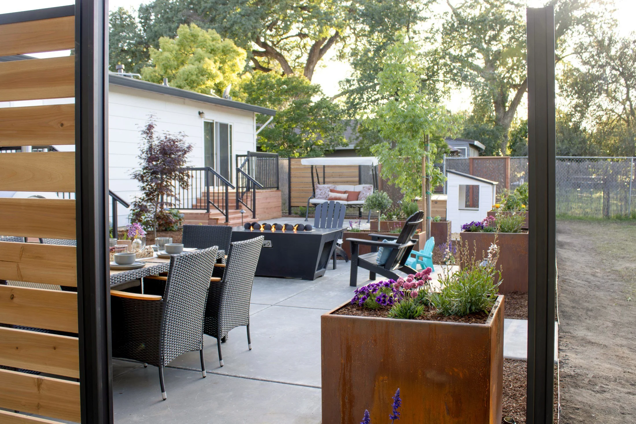 After: outdoor dining and a linear fire table on the new concrete patio, framed by cedar and steel privacy screens and raised Corten planters.