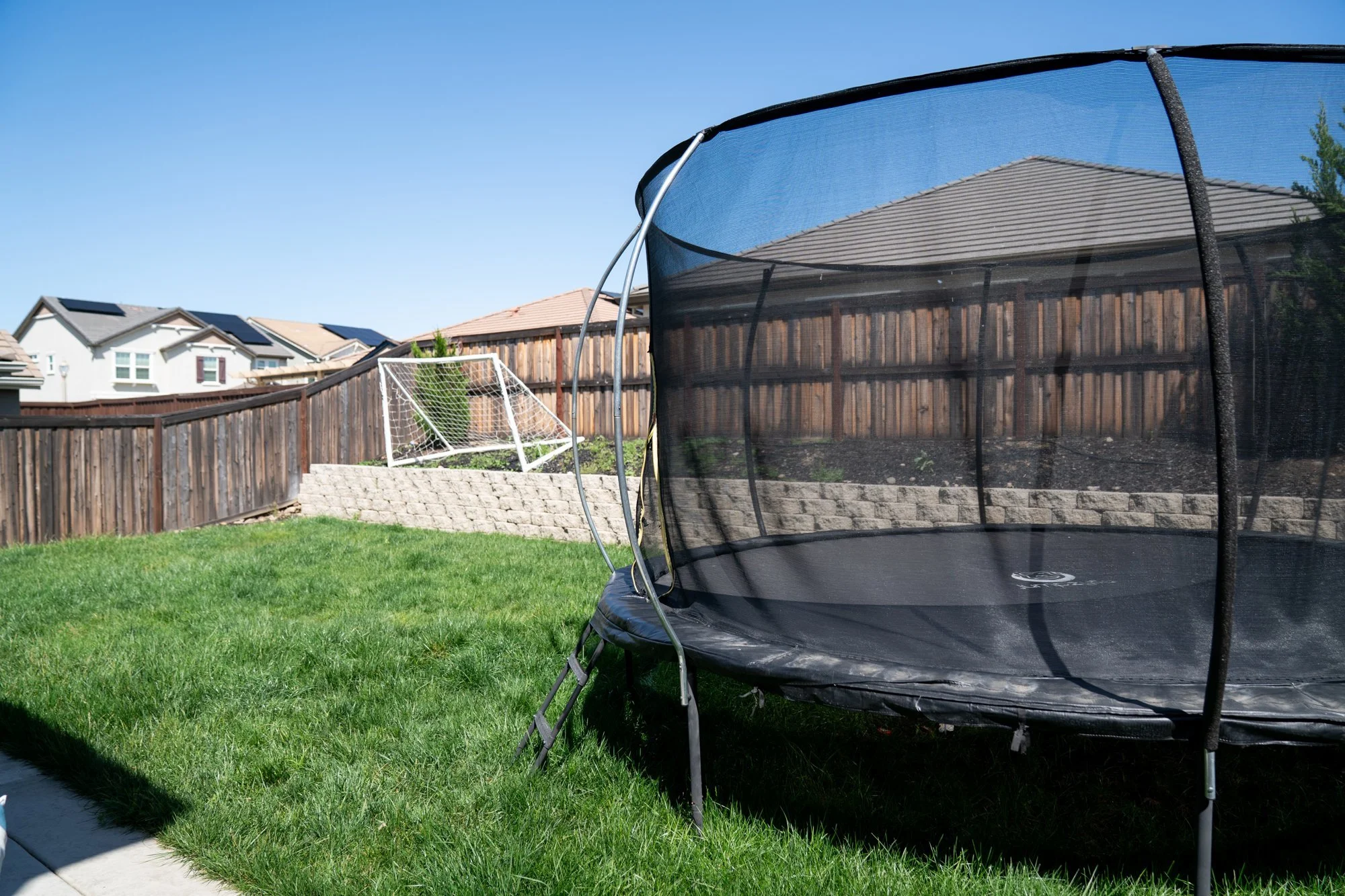 Before: a bare Roseville backyard with trampoline, patchy lawn, and empty fence lines prior to the HGTV Crashers renovation