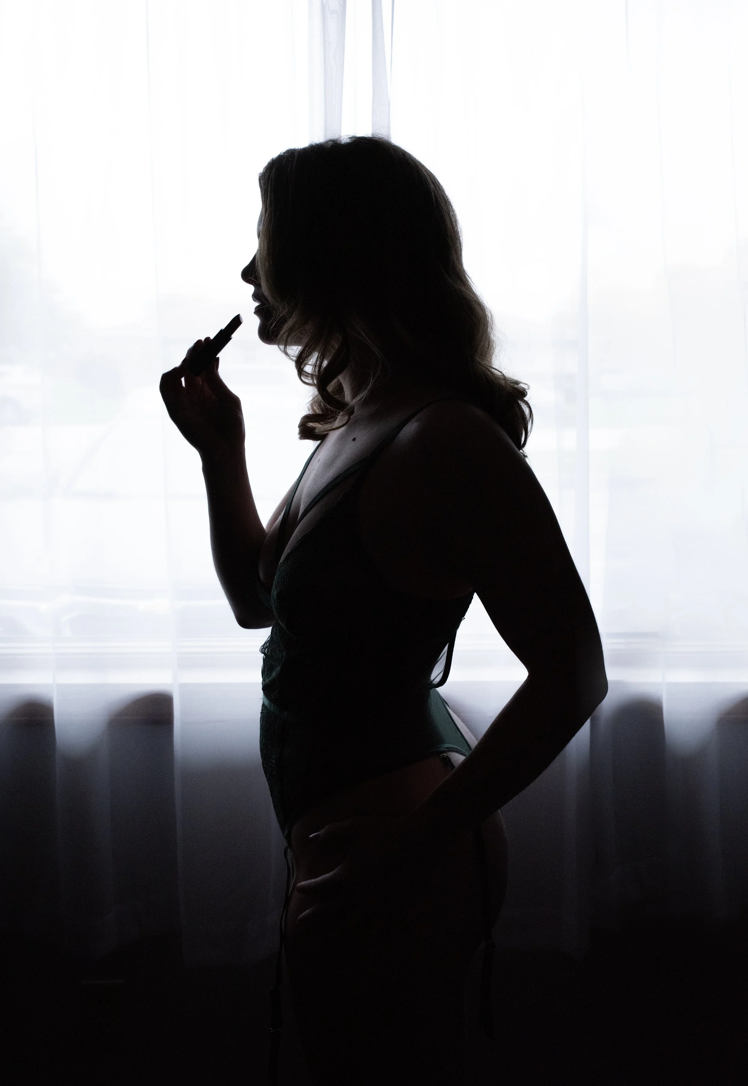 Silhouette of a woman applying lipstick in front of a sheer curtain.