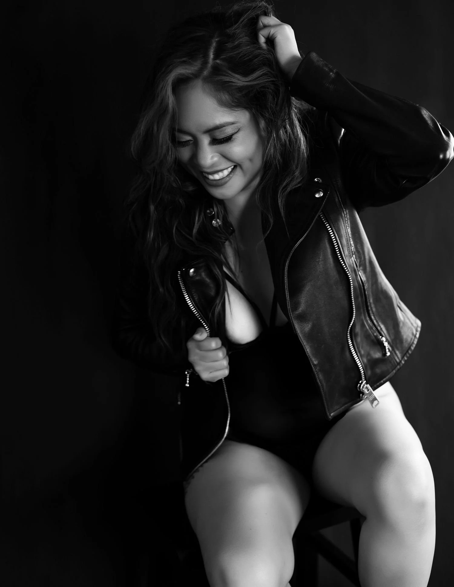 Smiling woman in leather jacket sitting, black and white photo.