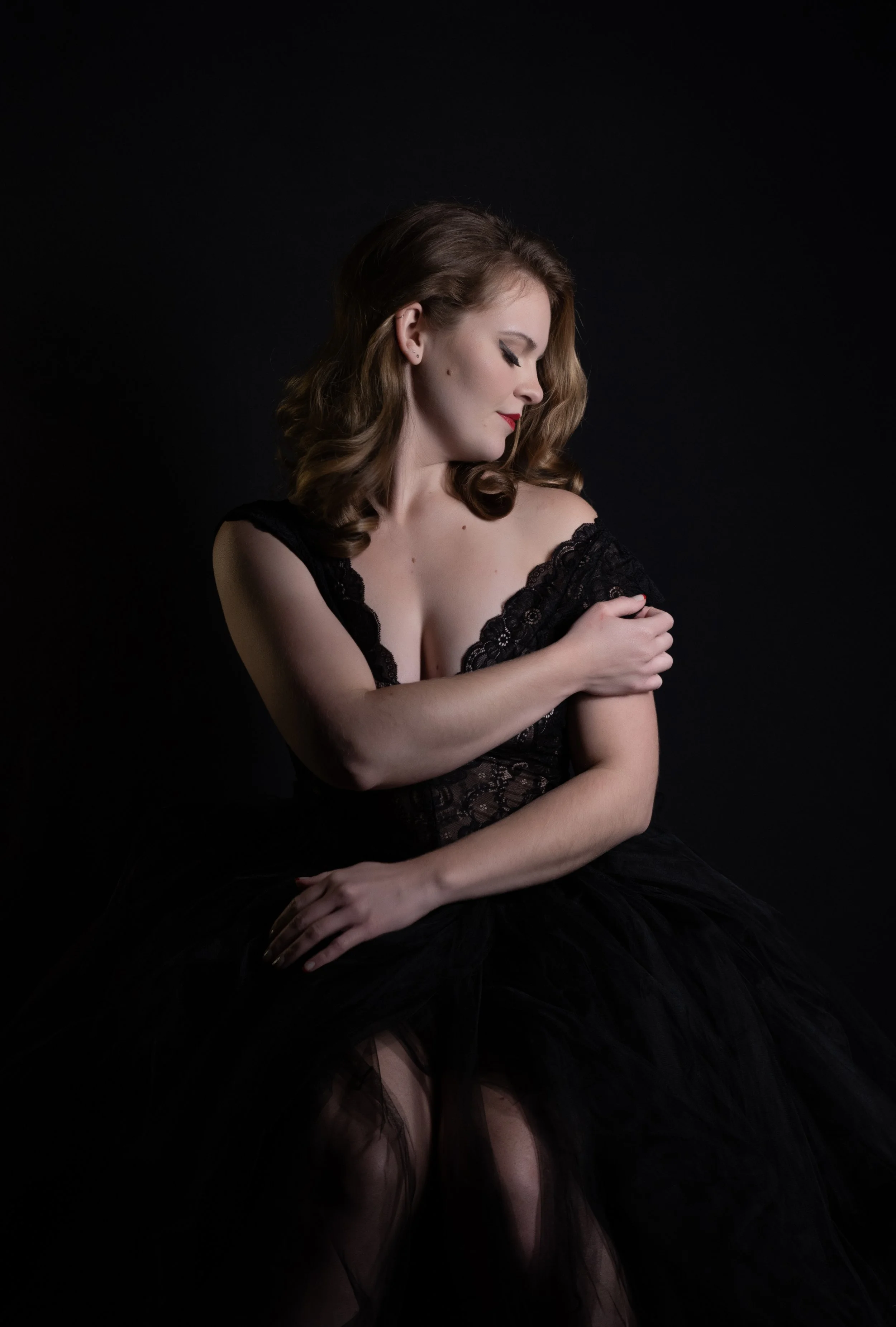 Woman in an elegant black dress posing against a dark background.