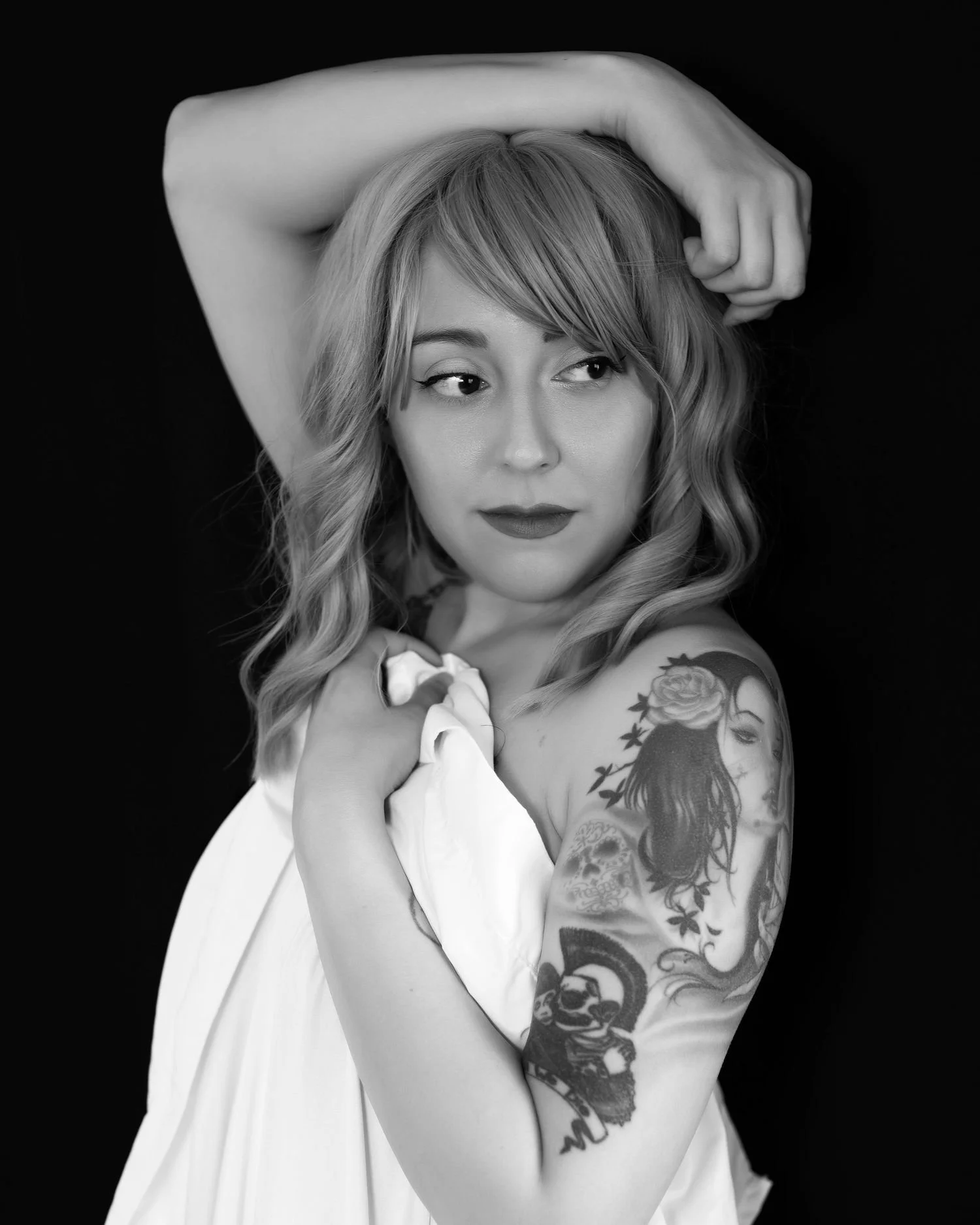 Black and white portrait of a woman with shoulder tattoo, draped in fabric, and looking to the side.