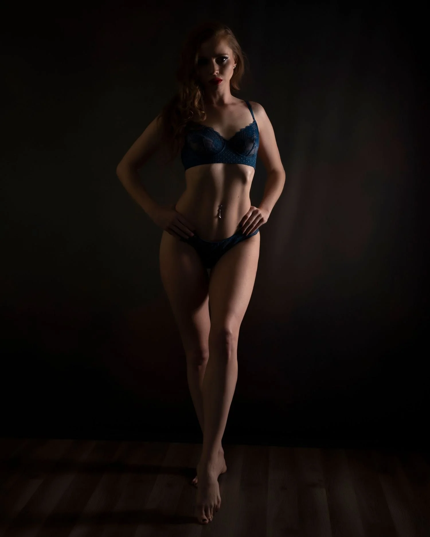 Silhouette of a woman wearing dark lingerie, posing against a dark background with hands on hips.