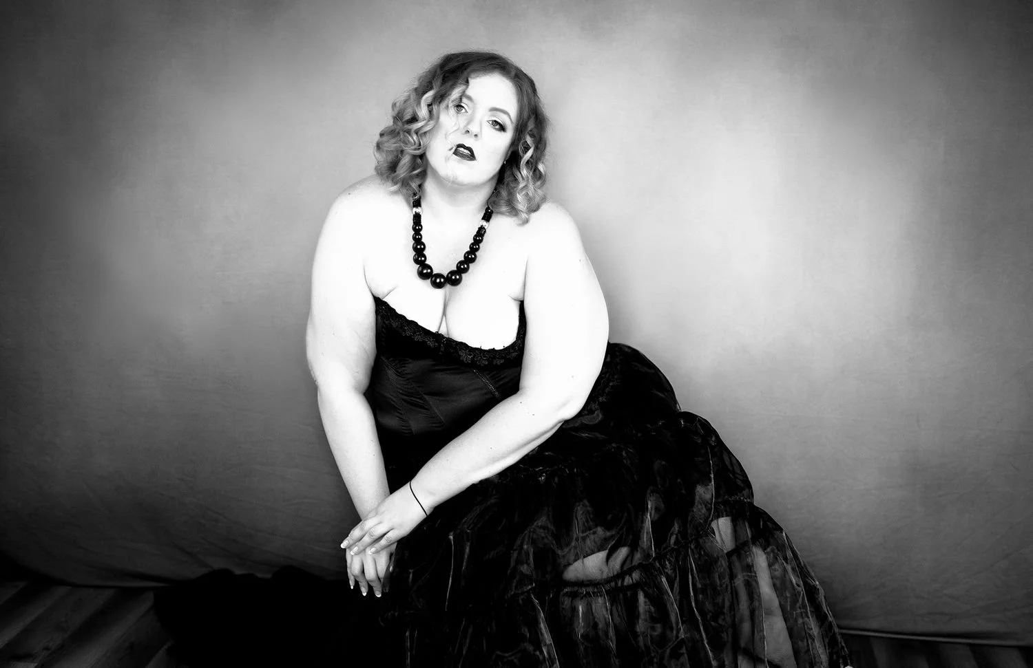 Black and white portrait of a person in a strapless dress and necklace, sitting against a plain background.