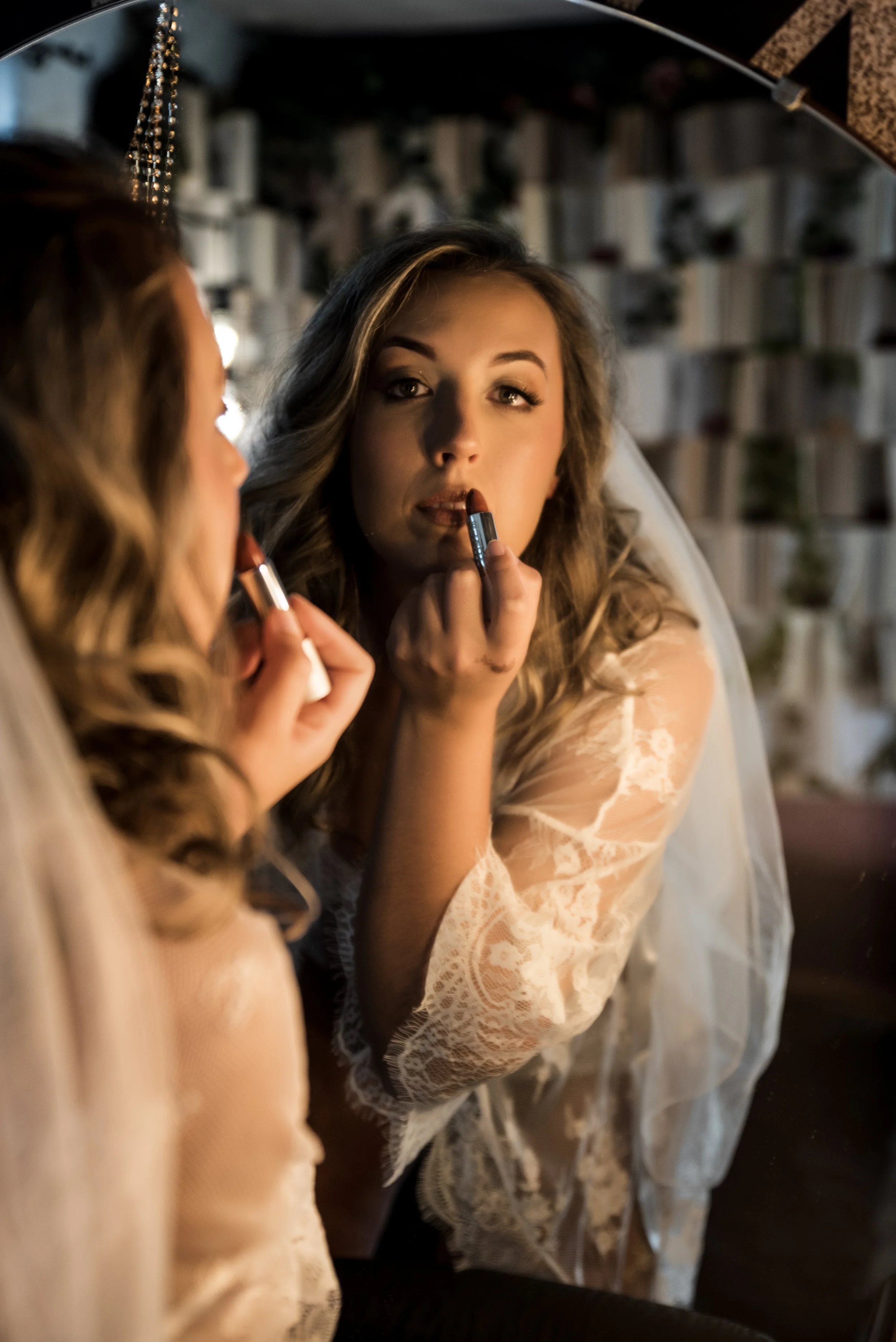 Bride wearing a veil putting lipstick on with a book wall in the background in a boudoir photography studio in Crown Point, Indiana.
