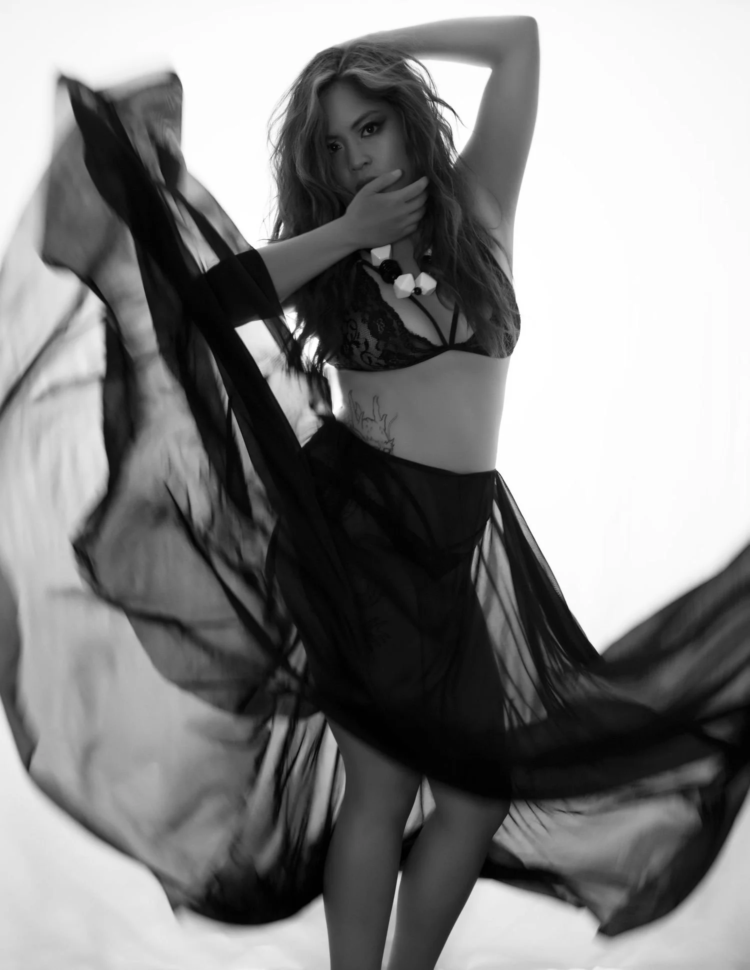 Black and white photo of a woman in a sheer outfit, striking a dynamic pose with flowing fabric.