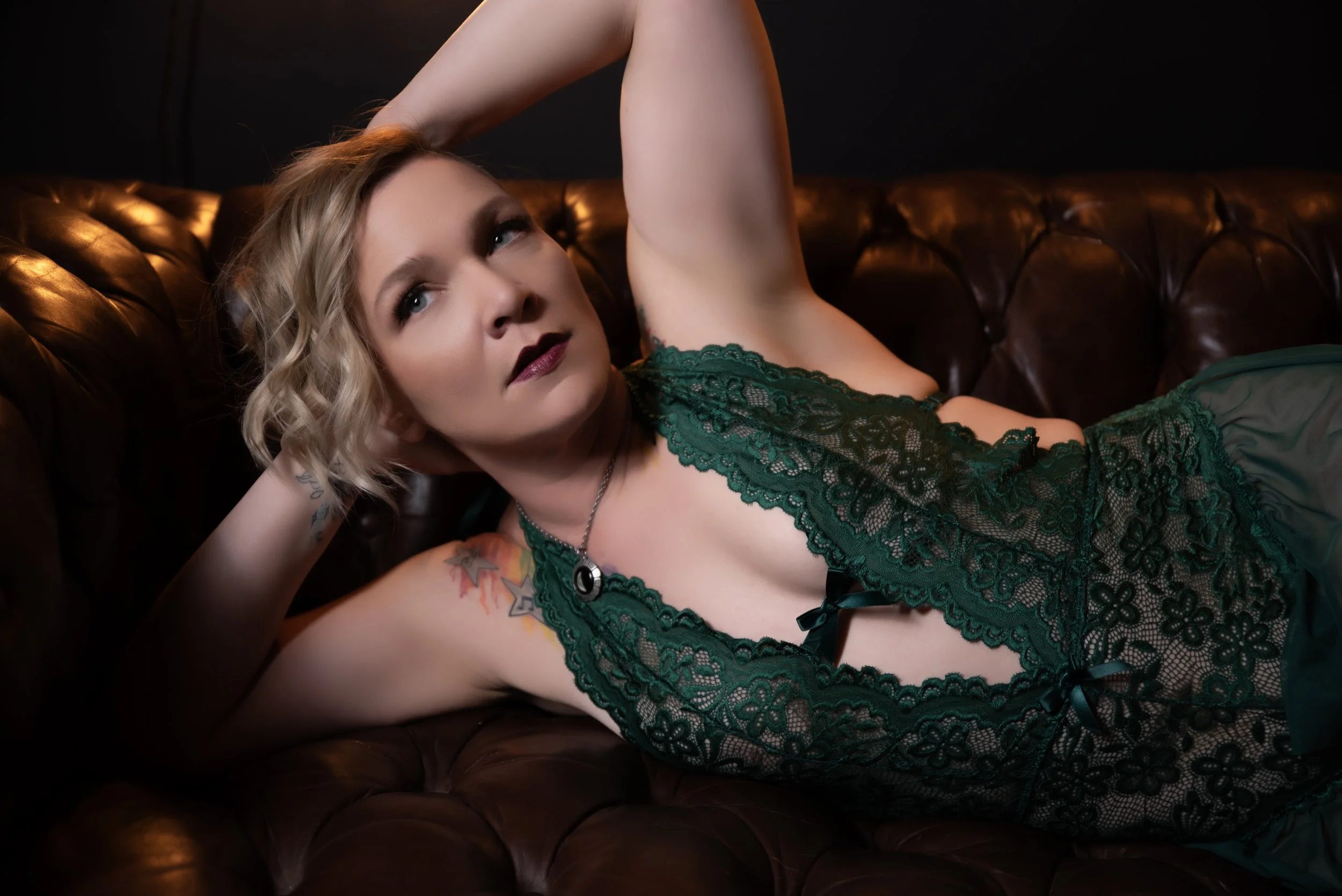Person lying on a brown leather sofa wearing a green lace outfit and looking upward.