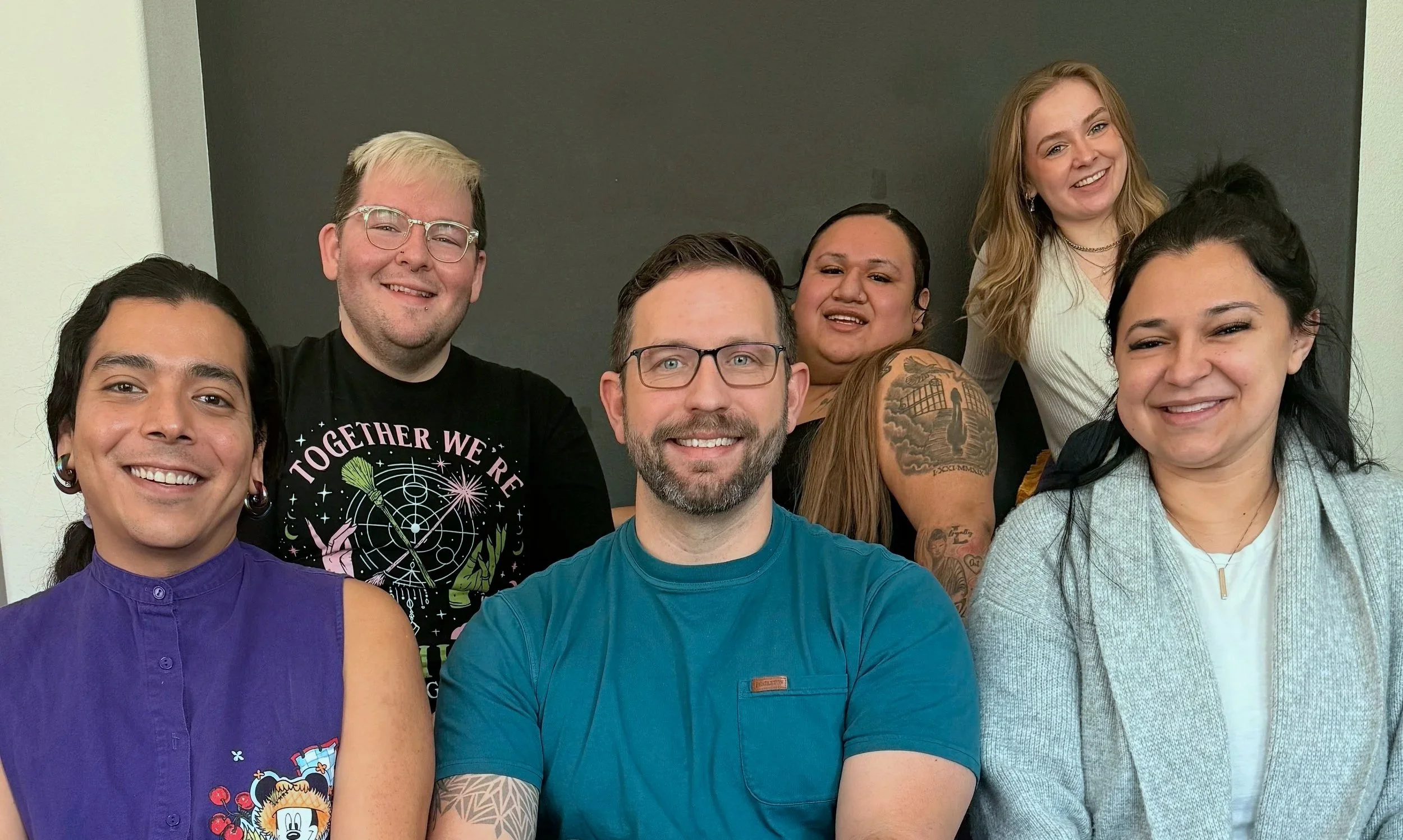 Six people posing in two rows, with three in front and three in back, standing in front of a black wall