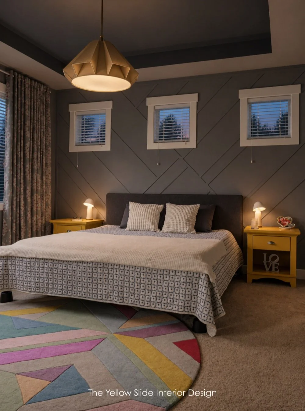 Color After Dark is a primary bedroom project where all walls, including the ceiling are drenched in a moody gray. The pops of color come through the rug, refinished nightstands and custom curtain panels. The pendant light creates just the right amou