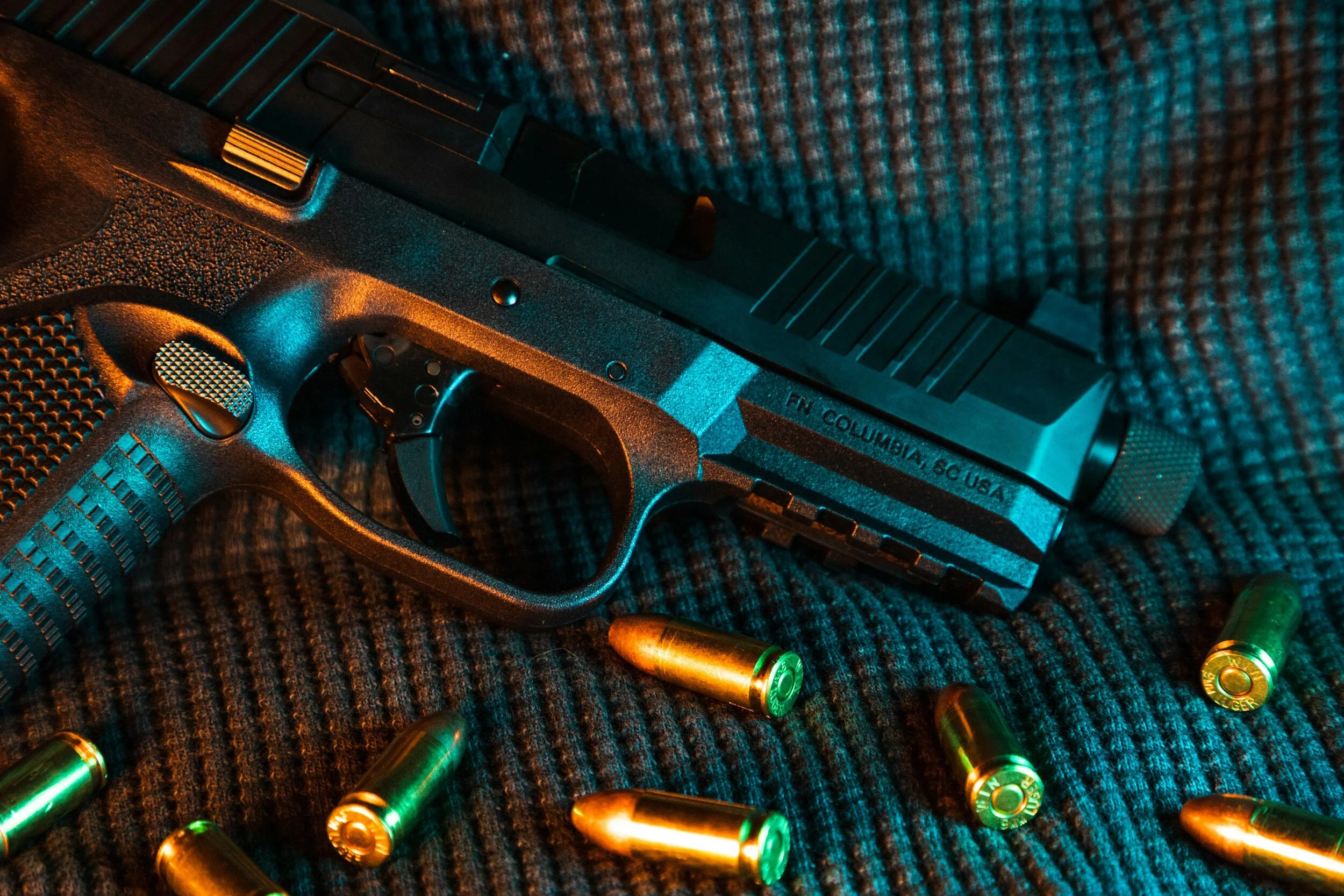 A handgun with a few bullets scattered on a textured fabric surface.