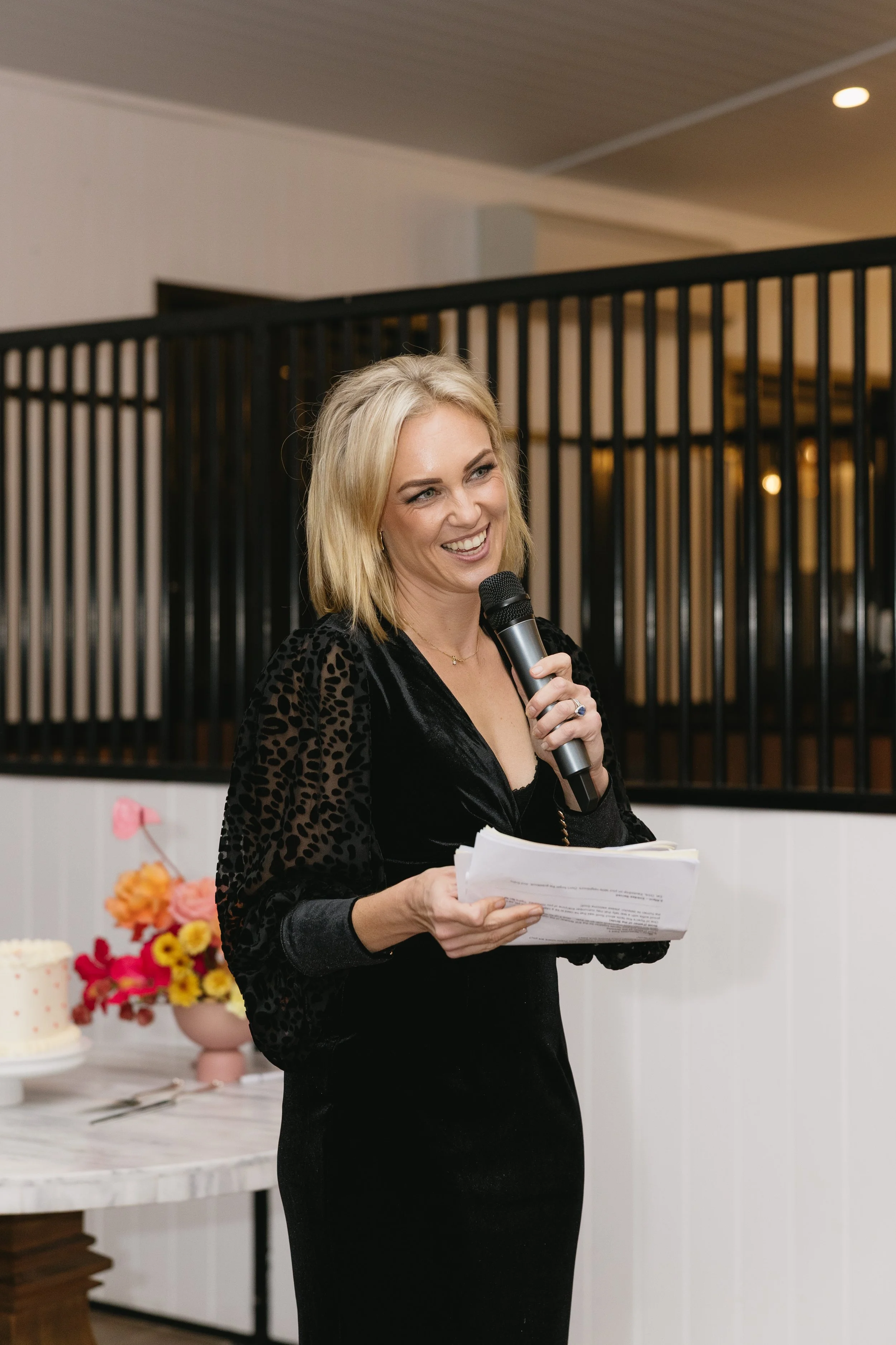 Bec Page, wedding celebrant and MC, speaking into the microphone at a wedding reception at Dark Horse Vineyard in the NSW Hunter Valley wine country. photo by Sarbo Studio