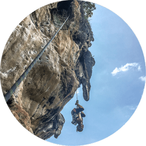 A person rock climbing on a steep cliff with a blue sky and some clouds in the background.