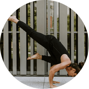 Person performing an arm balance yoga pose outdoors in front of vertical slats.
