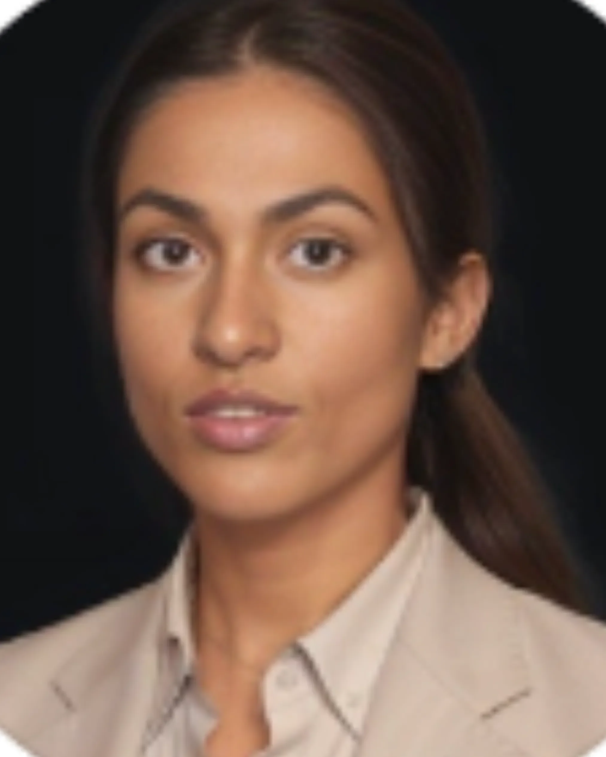 Close-up portrait of a young woman with straight dark hair, wearing a beige blazer and a white shirt, against a black background.