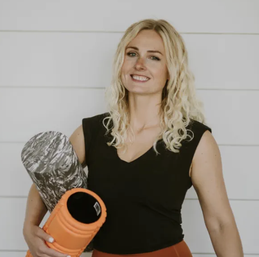Julia smiling and holding two different foam rollers in front of a white shiplap wall.