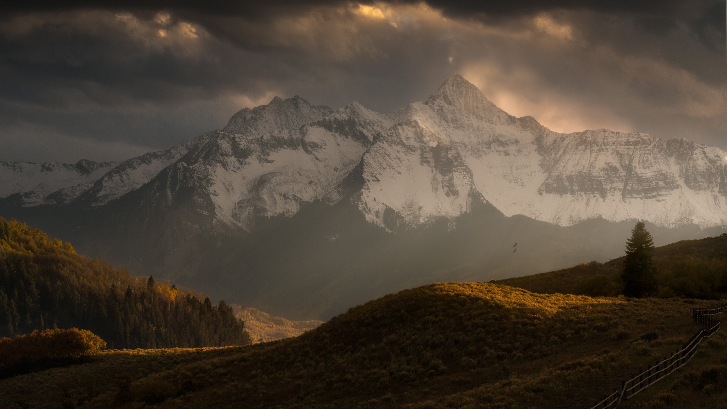 Storm clouds break over the snow-covered face of Wilson Peak above golden autumn hillsides near Telluride, Colorado.