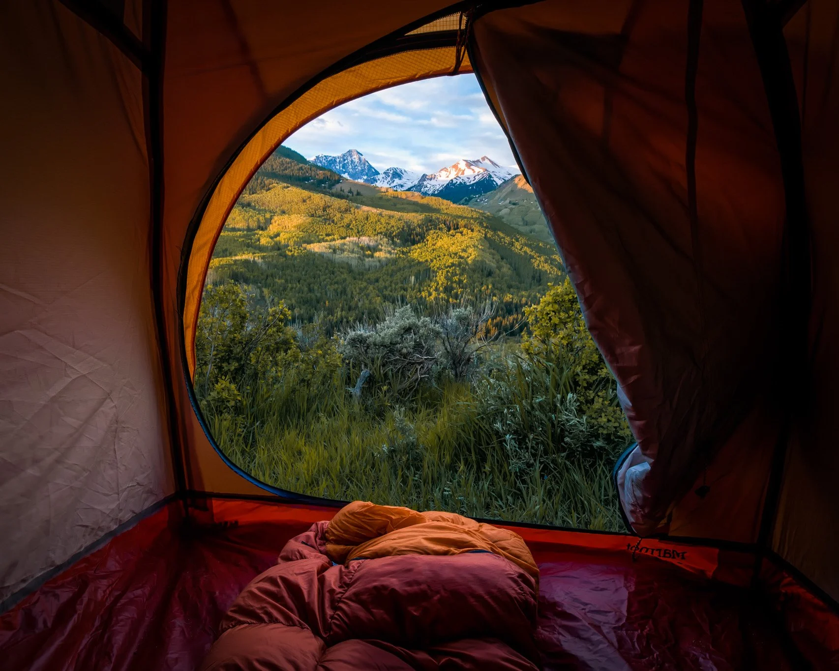 View from inside a tent through the open door, looking across sagebrush hills to snow-capped Capitol Peak, Colorado.