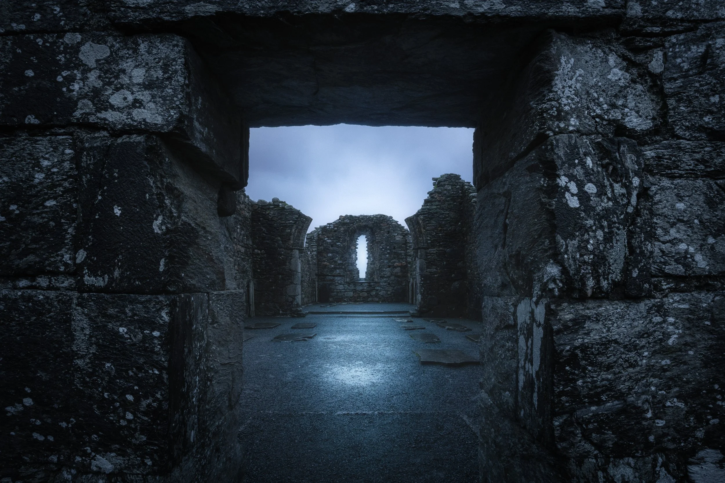 Looking through a stone doorway into the roofless cathedral ruins at Glendalough monastic site on a blue misty morning, County Wicklow, Ireland.