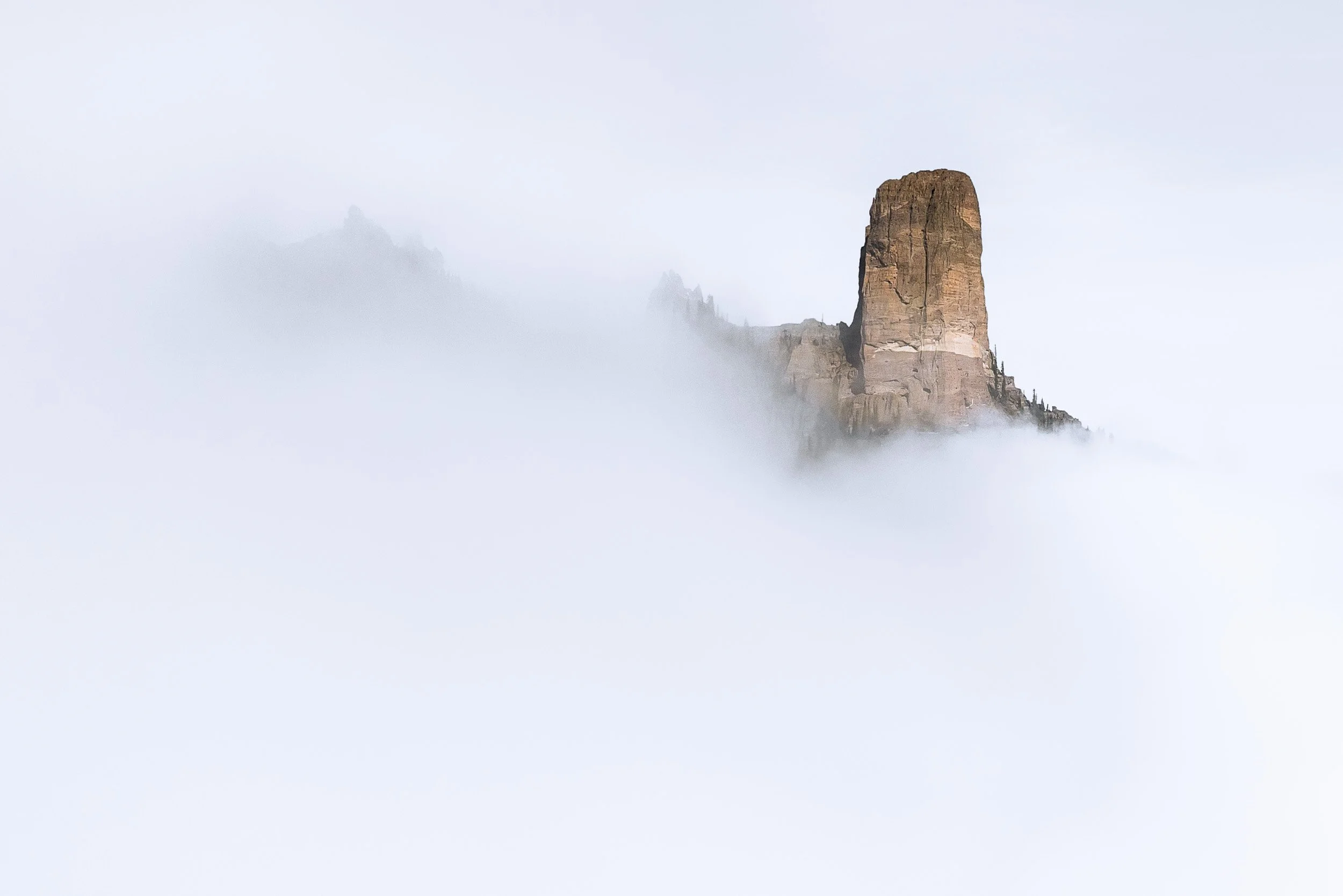 Chimney Rock emerges from a sea of white fog on the Cimarron Ridge near Owl Creek Pass, Colorado.
