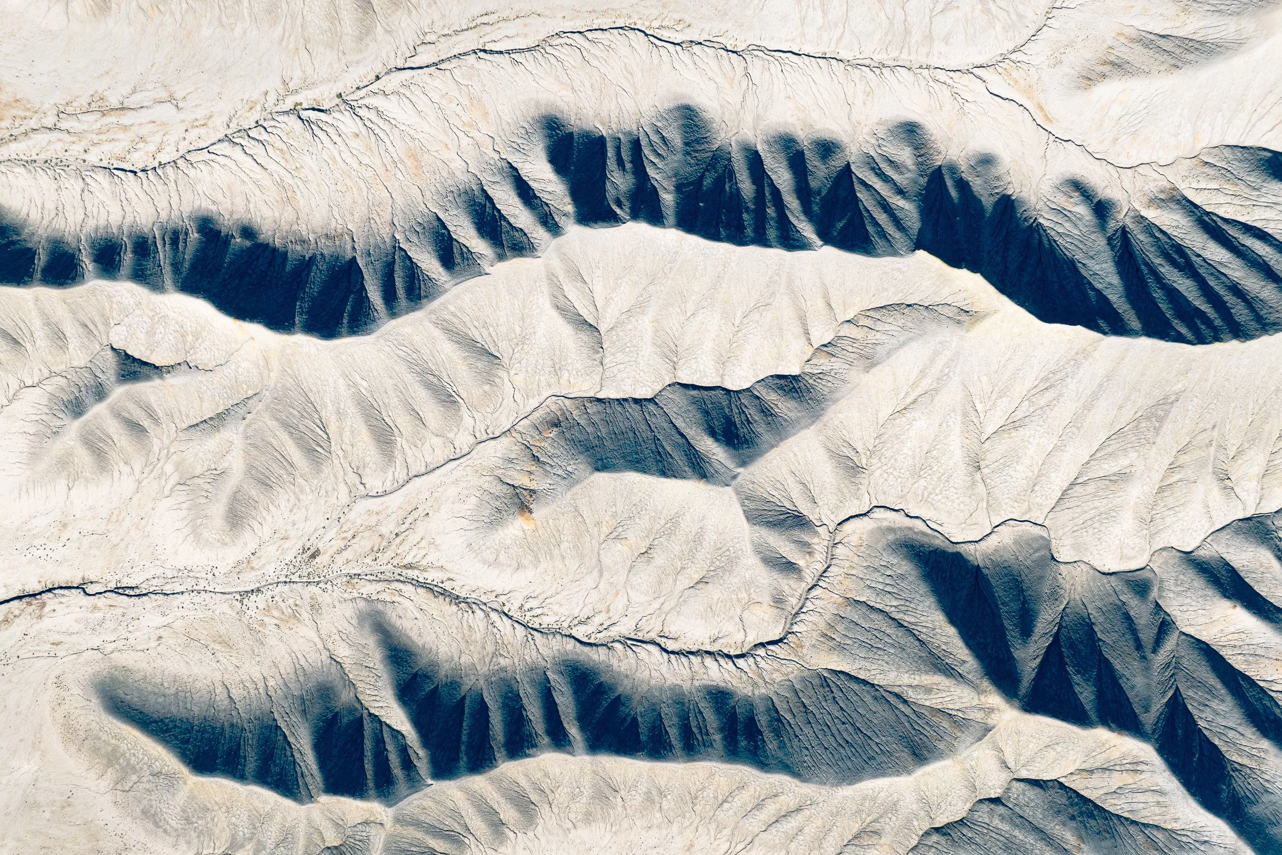 Aerial abstract of pale eroded desert ridges casting deep blue shadows, Utah.