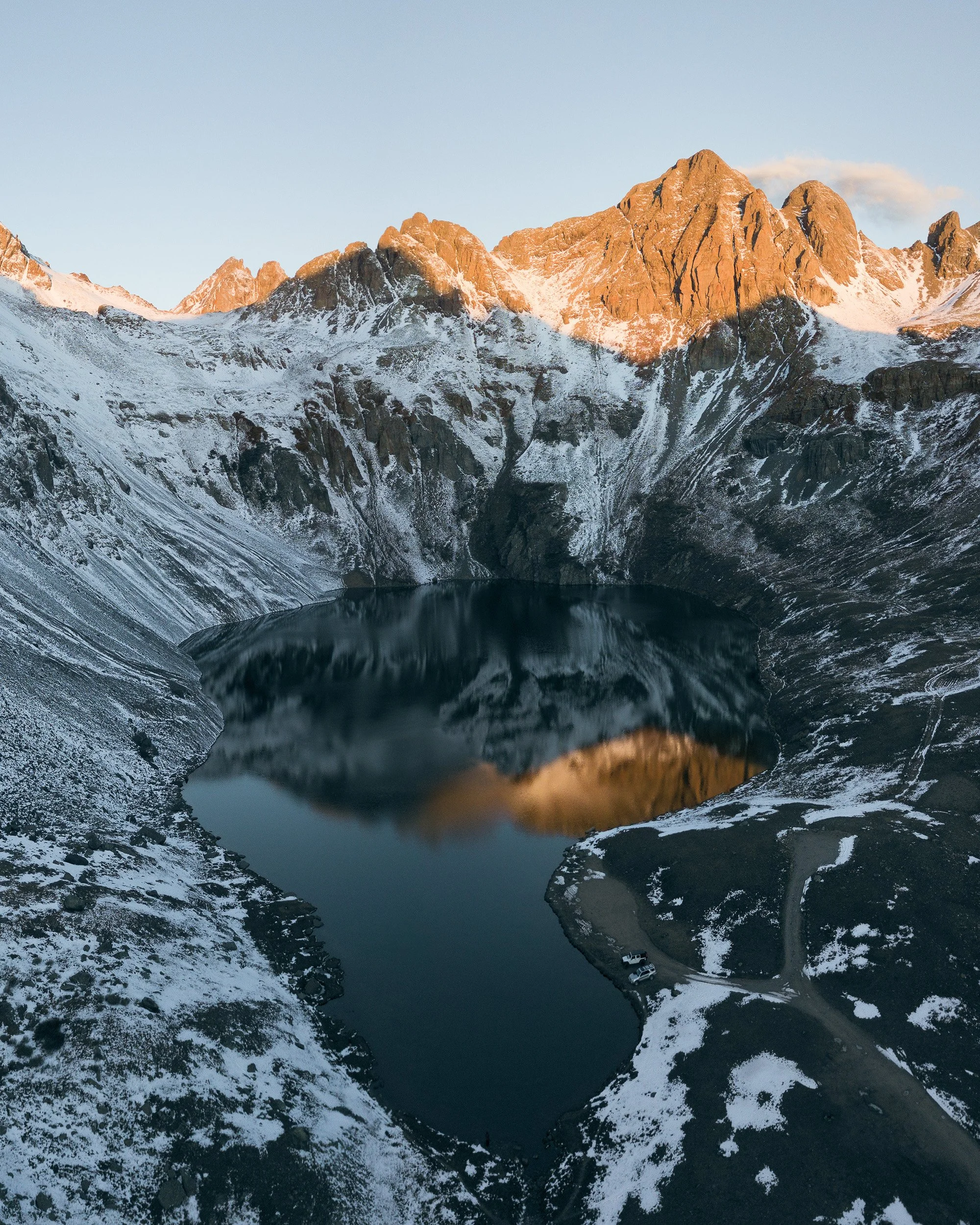 First light strikes snow-dusted peaks reflected in Clear Lake, seen from the air outside of Silverton, Colorado.