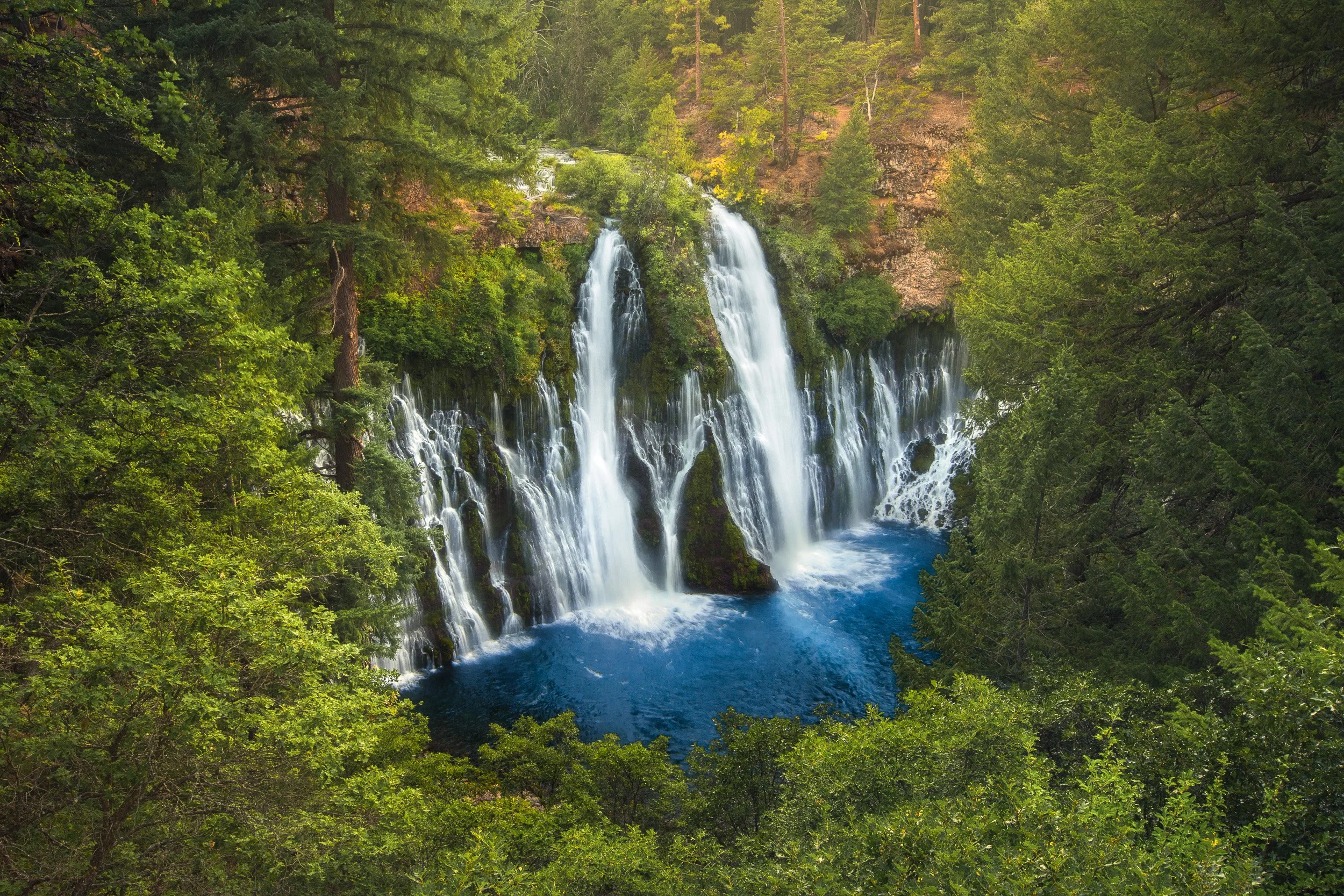 Burney Falls pours over a mossy cliff in dozens of spring-fed cascades into a deep blue pool at McArthur-Burney Falls Memorial State Park, California.