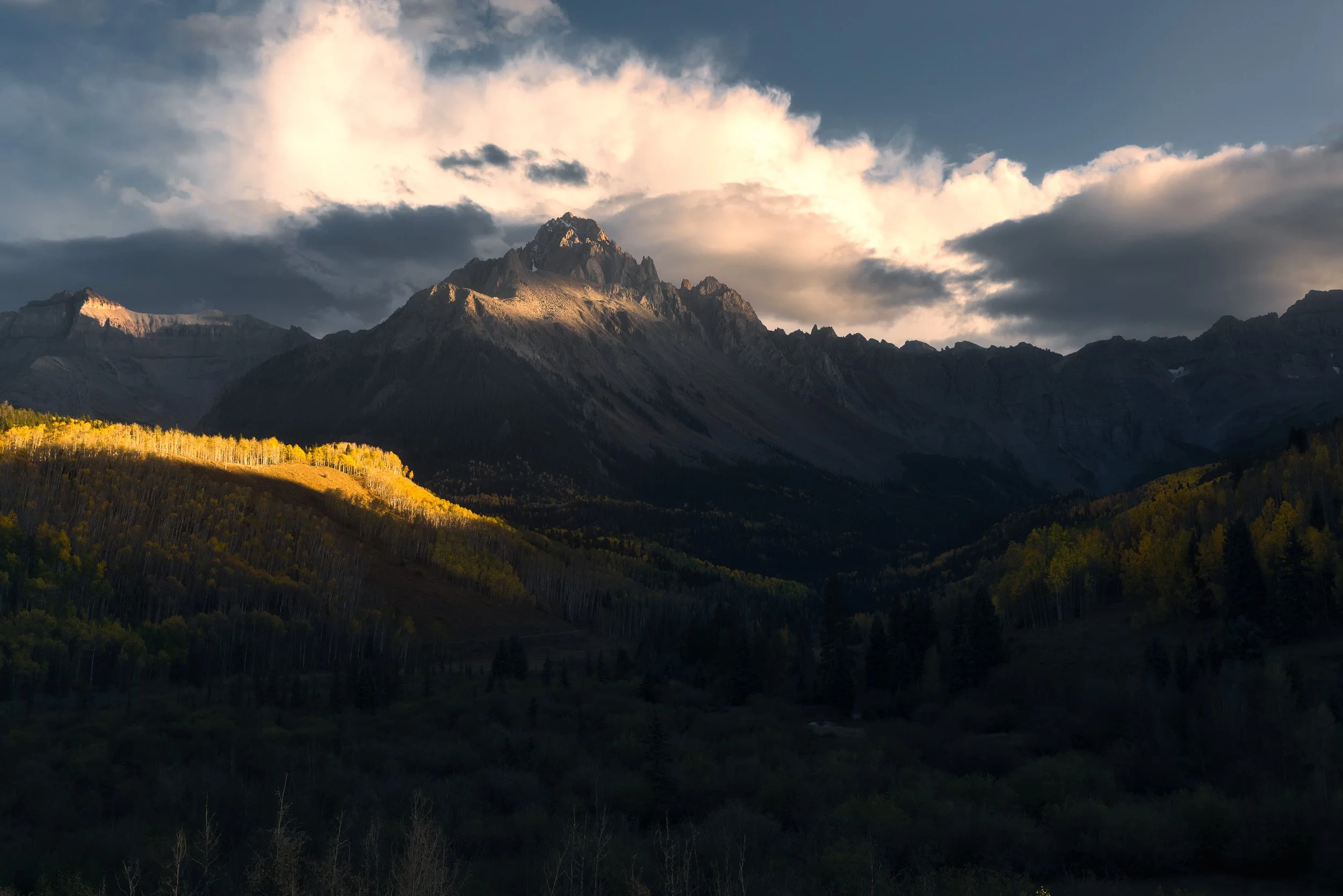 A band of sunlight ignites golden aspens below the shadowed face of Mount Sneffels, near Dallas Divide, Colorado.