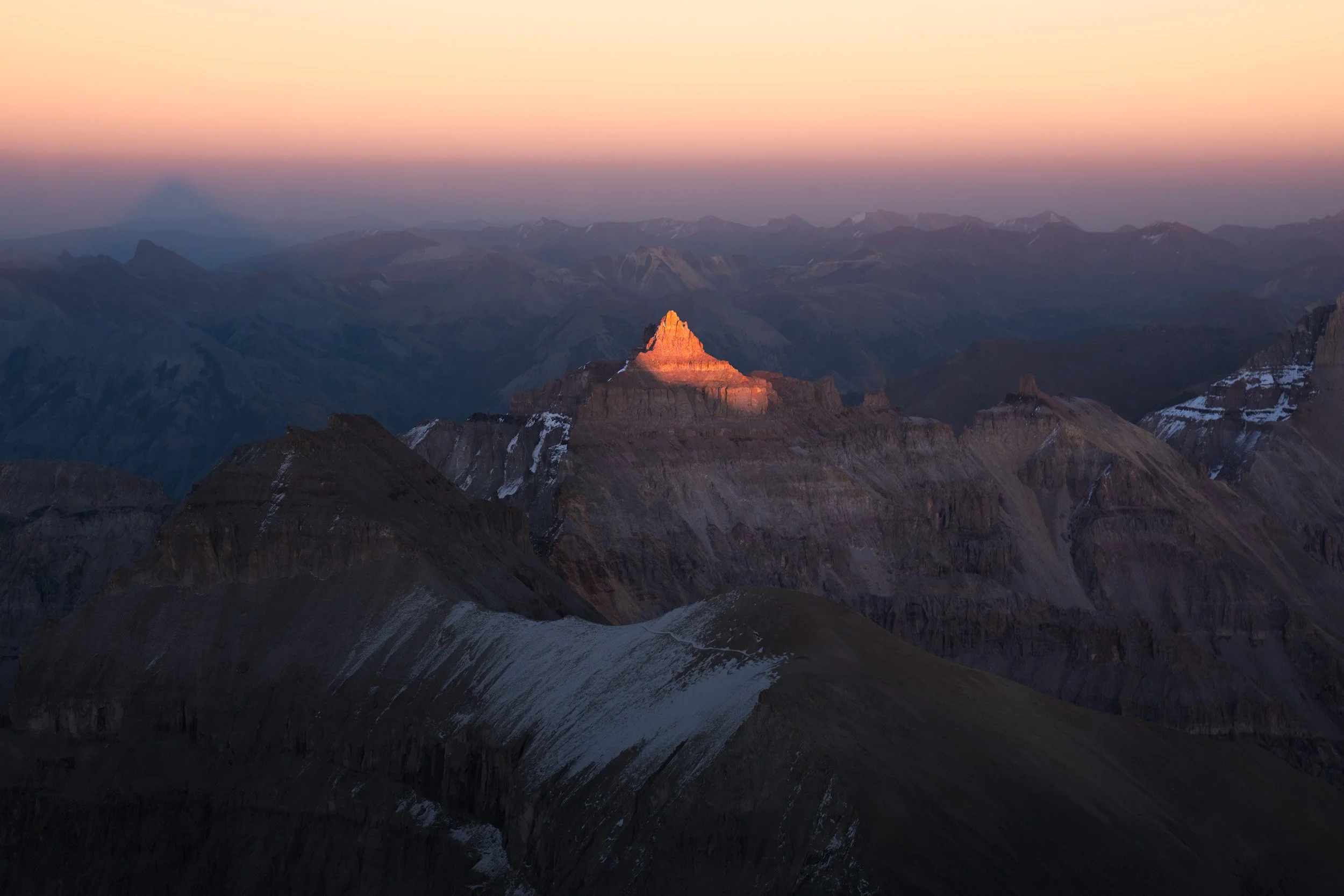 Last light ignites a Teakettle Mountain above layers of blue dawn haze in the San Juan Mountains, Colorado.