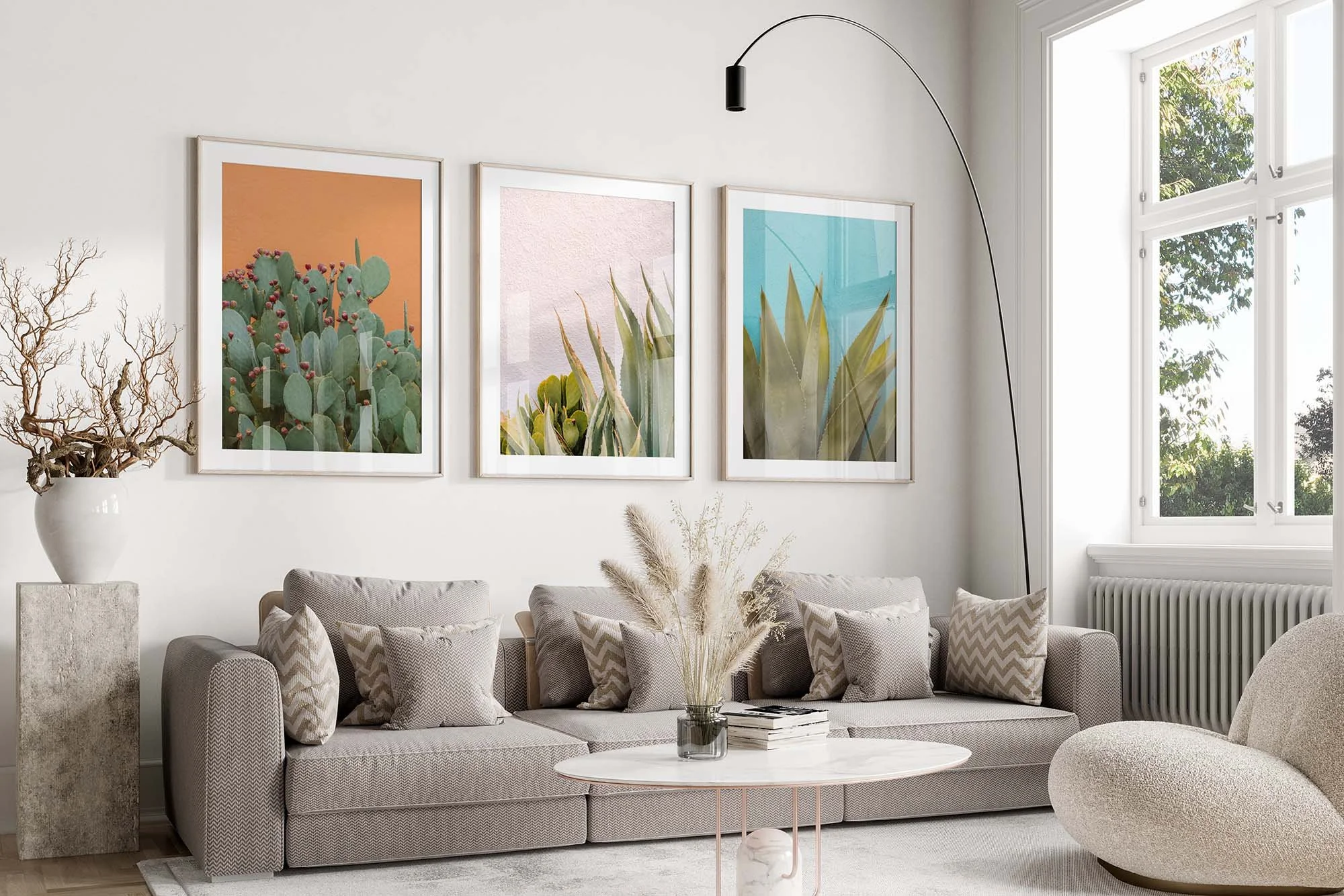 Set of three framed desert botanical prints — prickly pear cactus on orange, agave on blush pink, and agave on turquoise — hung above a gray sofa in a bright living room