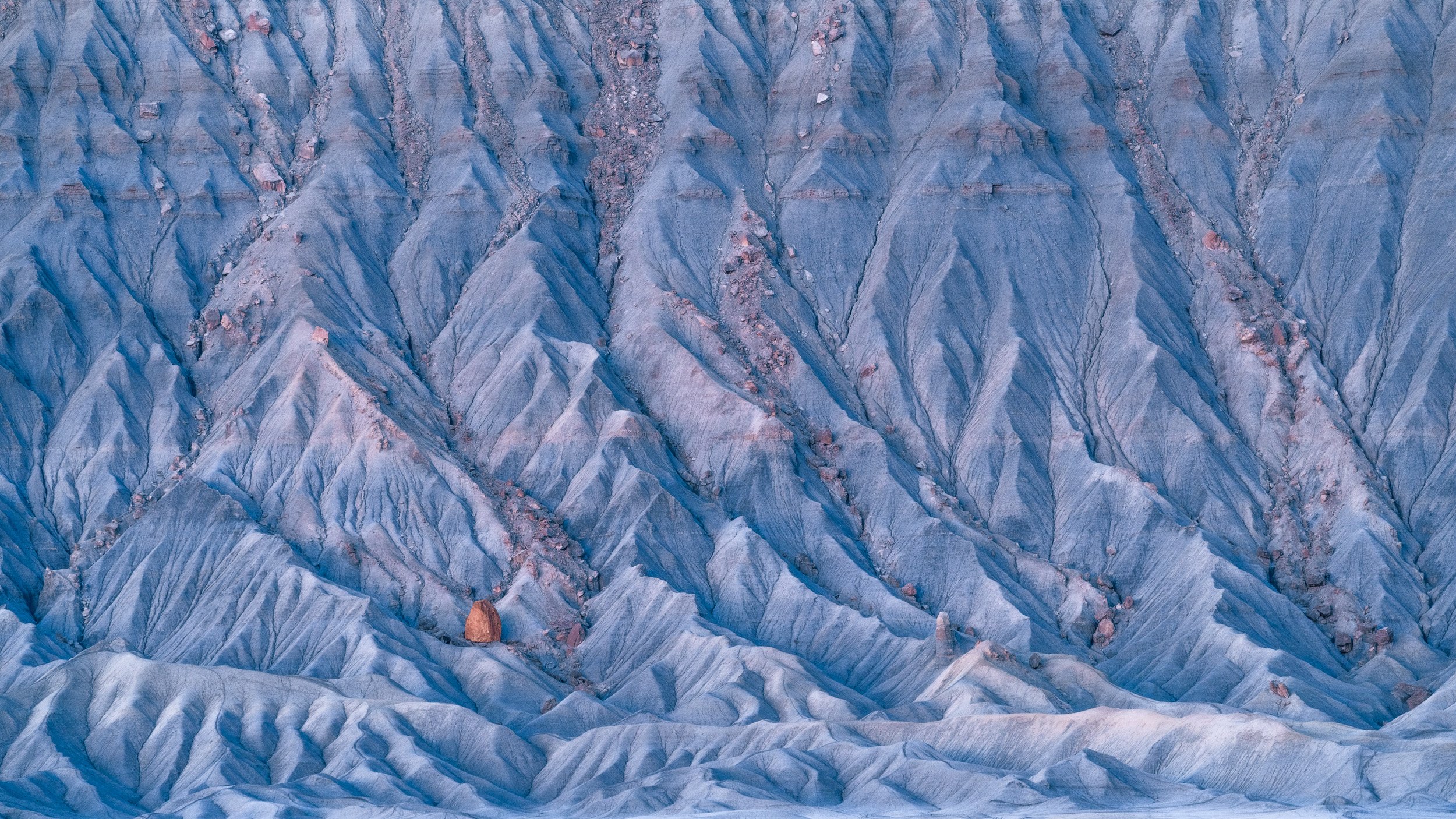 A single orange boulder rests among blue-grey badland ridges in soft twilight, Hanksville, Utah.