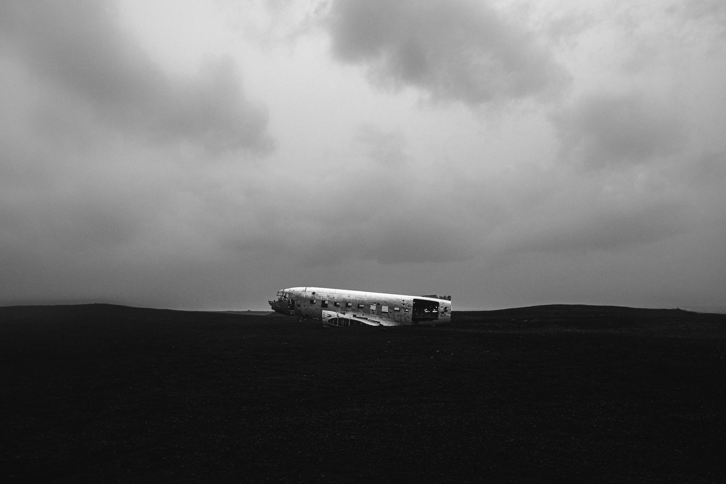 The abandoned DC-3 plane wreck rests on the black sand of Sólheimasandur under a heavy gray sky, South Iceland.