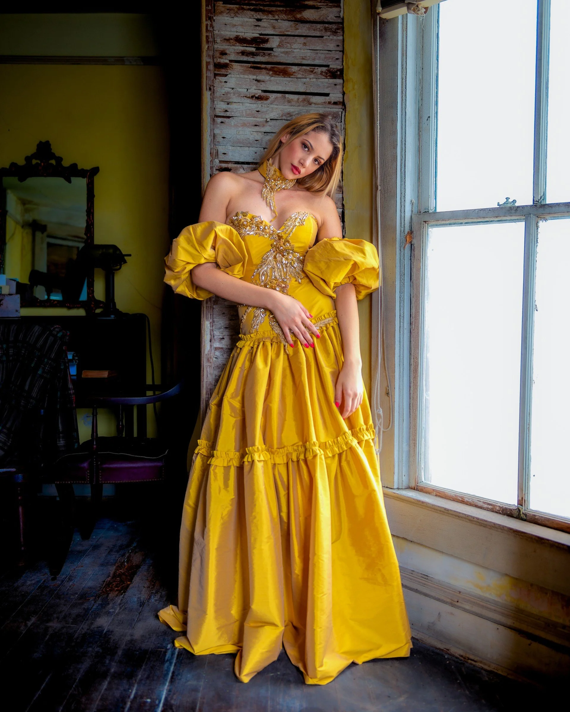 Model wearing a yellow Aurelia Batista gown beside a window and weathered door. Photography by Zech Browning.