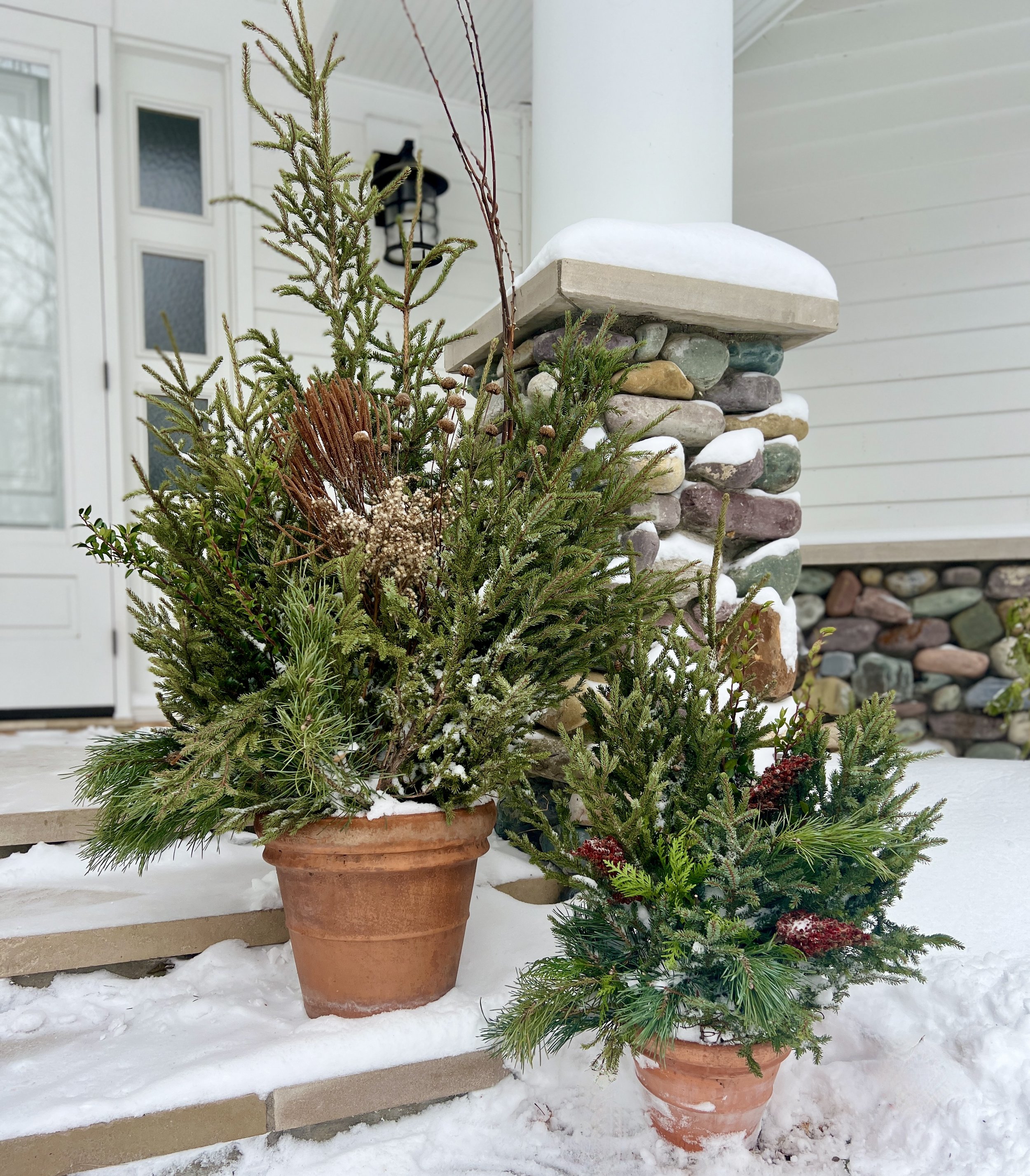 Naturalistic winter greenery planters in front of a white house.