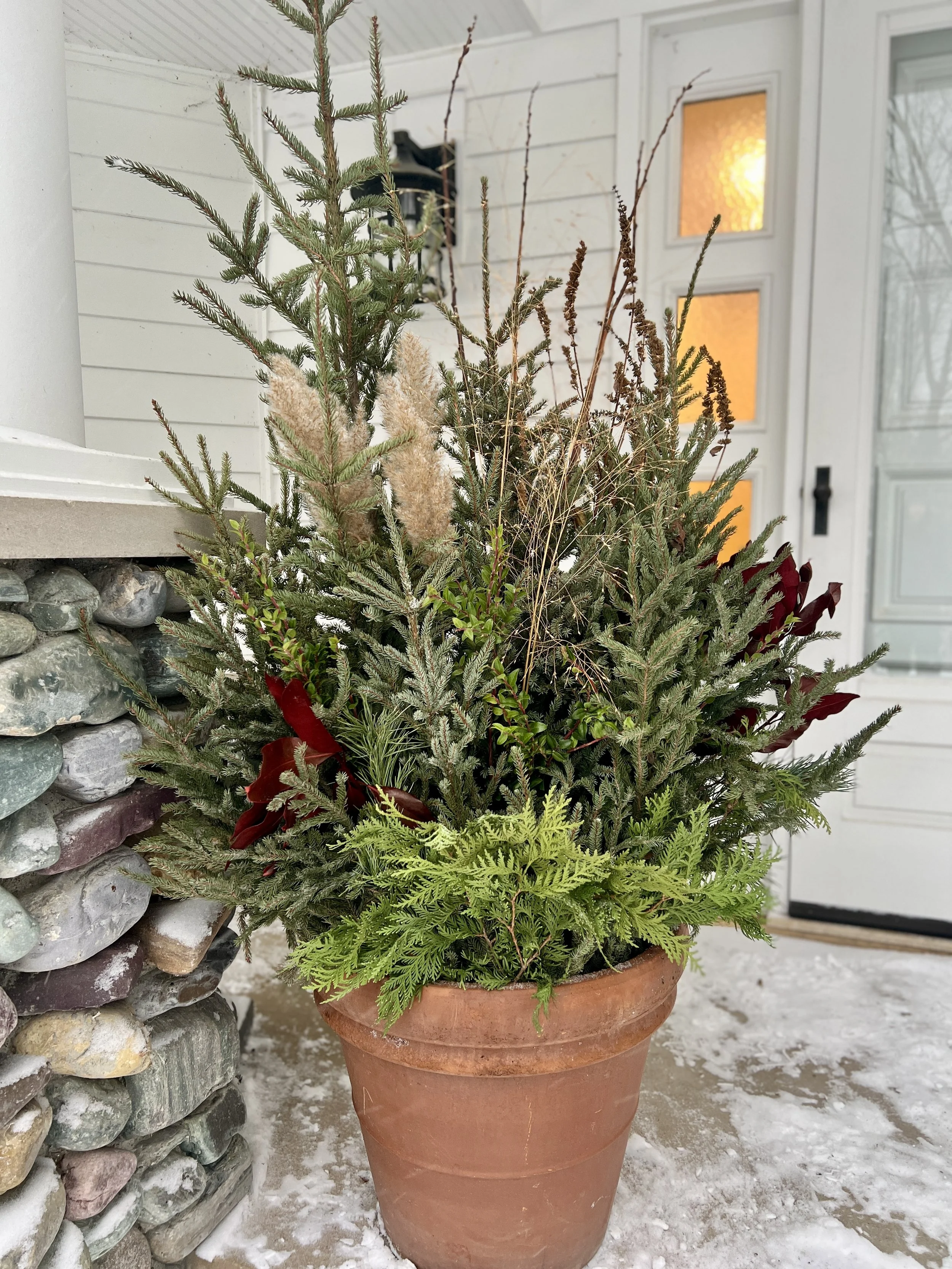 Naturalistic winter greenery planters in front of a white house.