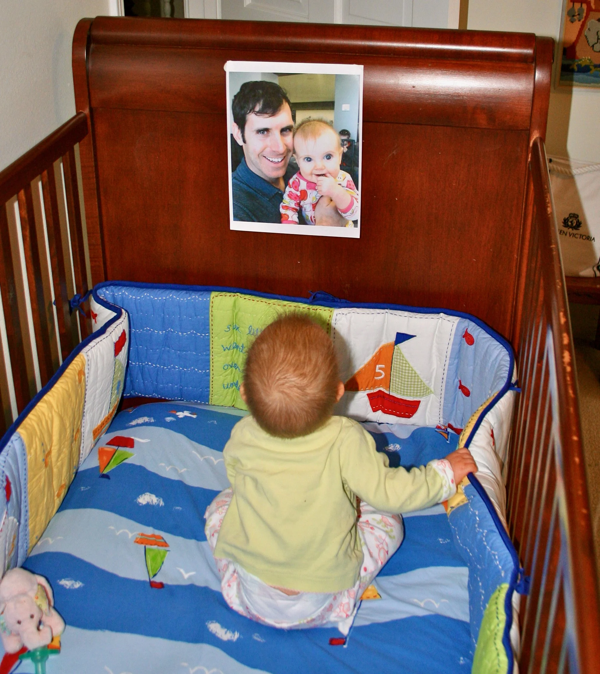 A baby in a crib looks up at a photo of her father.